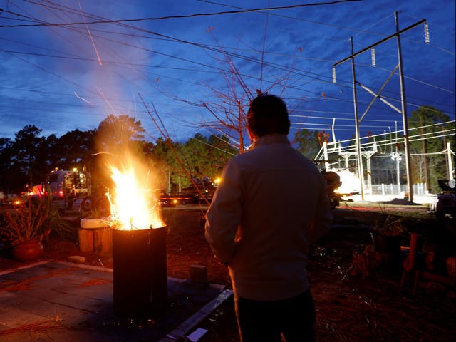 <p>A man warms himself in front of a makeshift fire as he watches Duke Energy personnel work to restore power at a crippled electrical substation in Moore County, North Carolina</p>