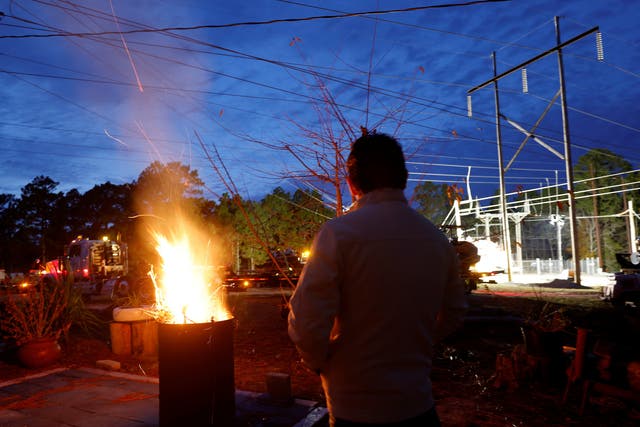 <p>A man warms himself in front of a makeshift fire as he watches Duke Energy personnel work to restore power at a crippled electrical substation in Moore County, North Carolina</p>