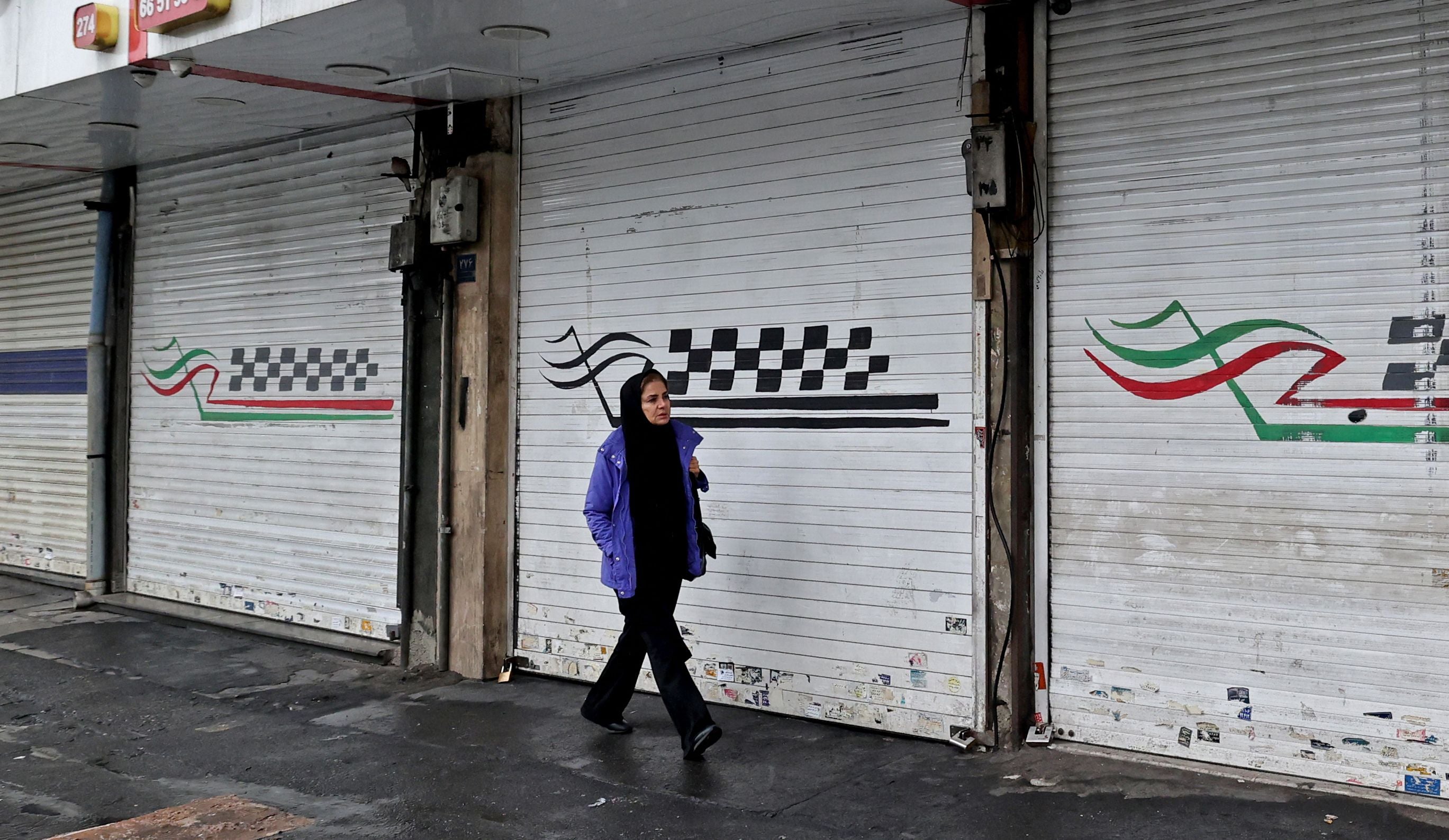 A woman walks past a closed shop along Satarkhan street in Iran's capital Tehran