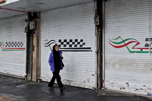 <p>A woman walks past a closed shop along Satarkhan street in Iran's capital Tehran</p>