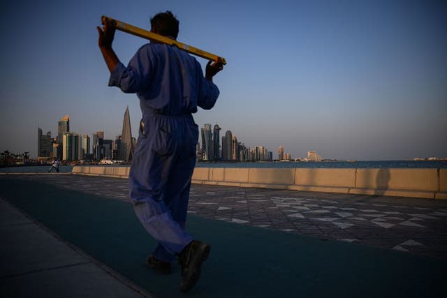 <p>Un trabajador camina por la Corniche de Doha con el West Bay en el fondo </p>