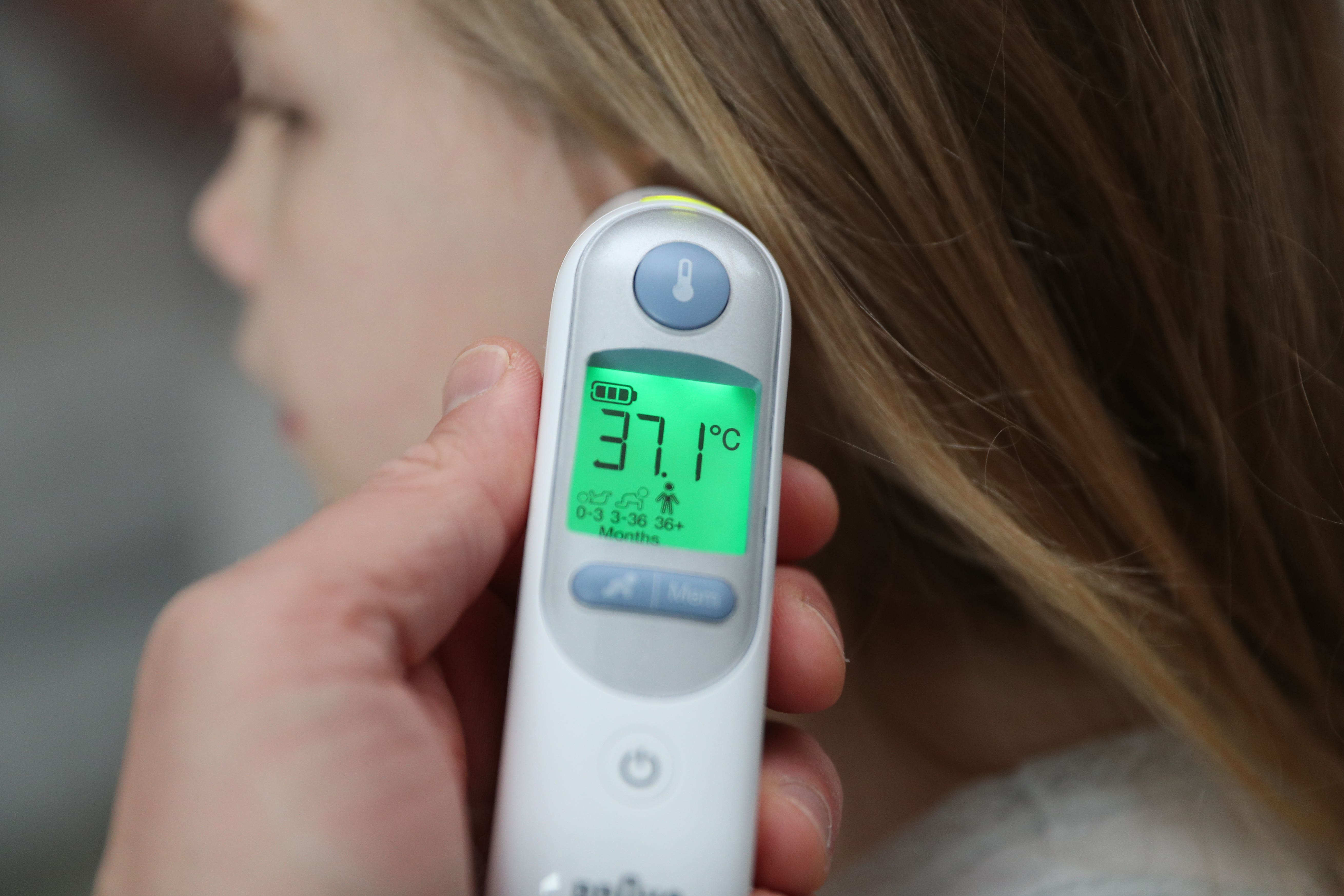 A child’s temperature of 37.1 degrees is taken using an ear thermometer. A high temperature (38C and above) can be a sign of Strep A infection (PA)