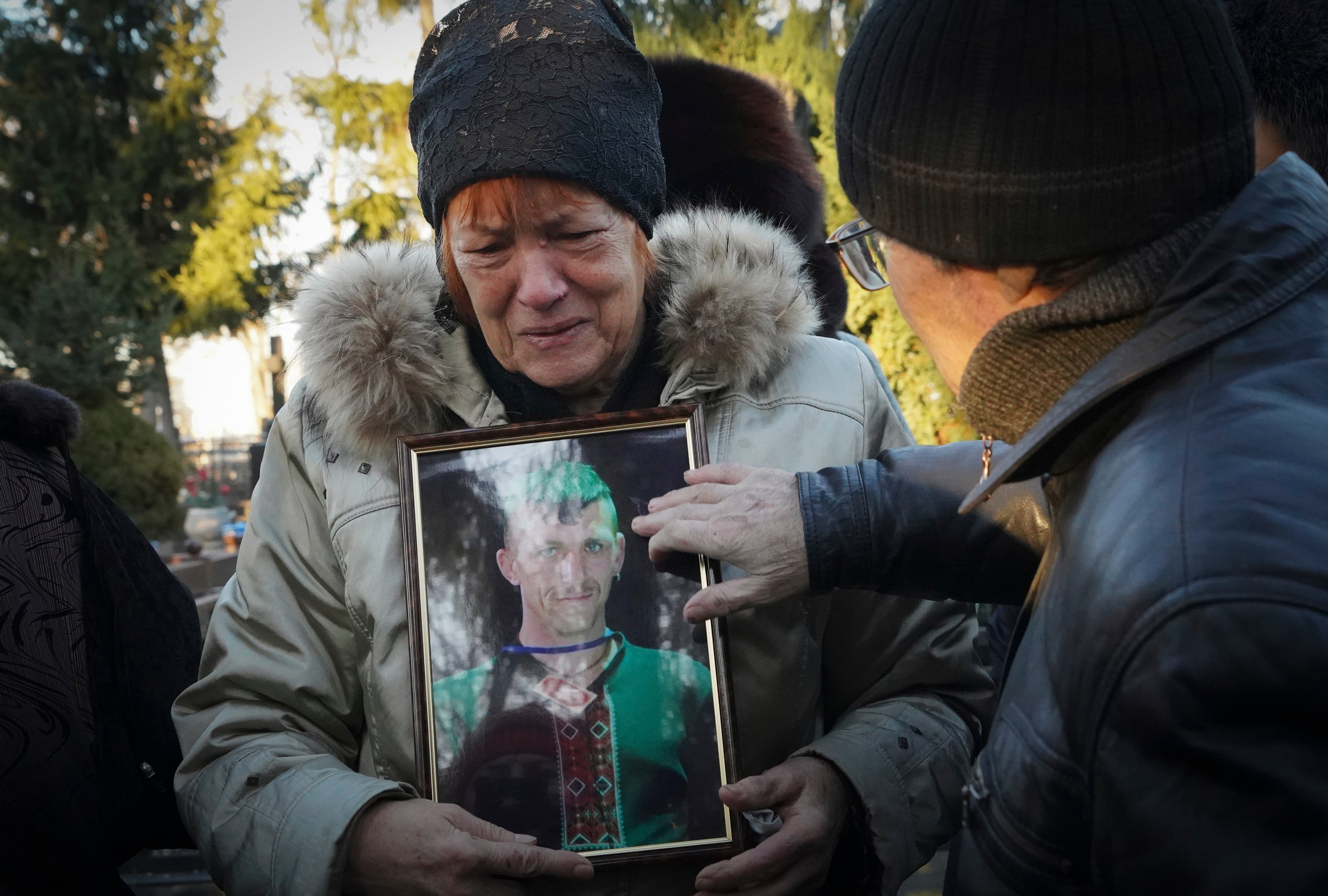 The mother of Ukrainian children’s writer Volodymyr Vakulenko holds his photo near his grave in Kharkiv on Tuesday