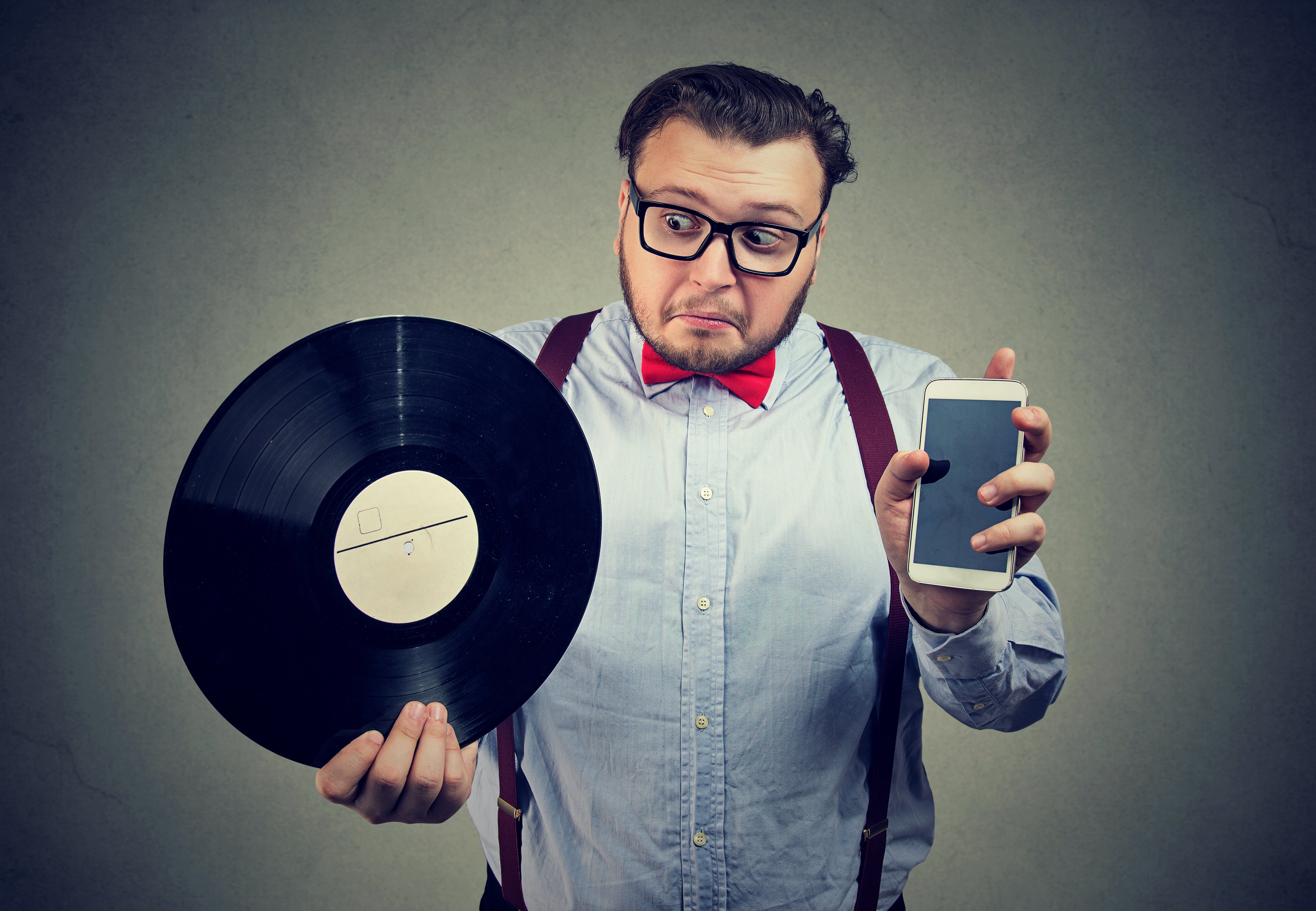 Man holding vinyl record and smartphone comparing old and new.