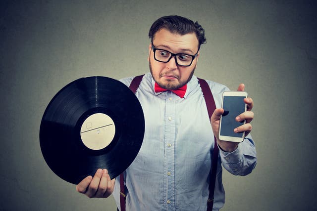 <p>Man holding vinyl record and smartphone comparing old and new.</p>