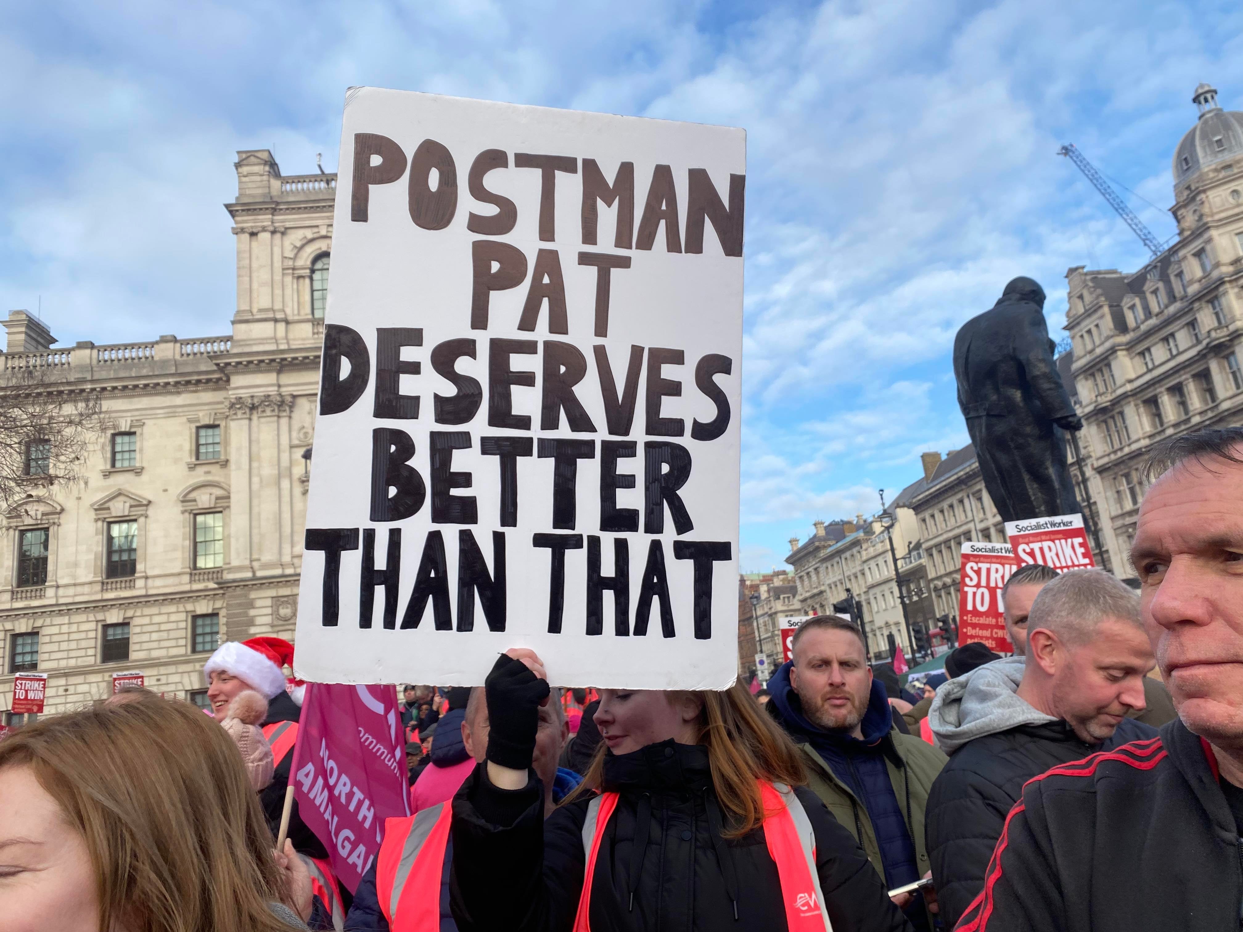 Striking postal worker holds placard reading ‘Postman Pat deserves better than that’ at Parliament Square rally