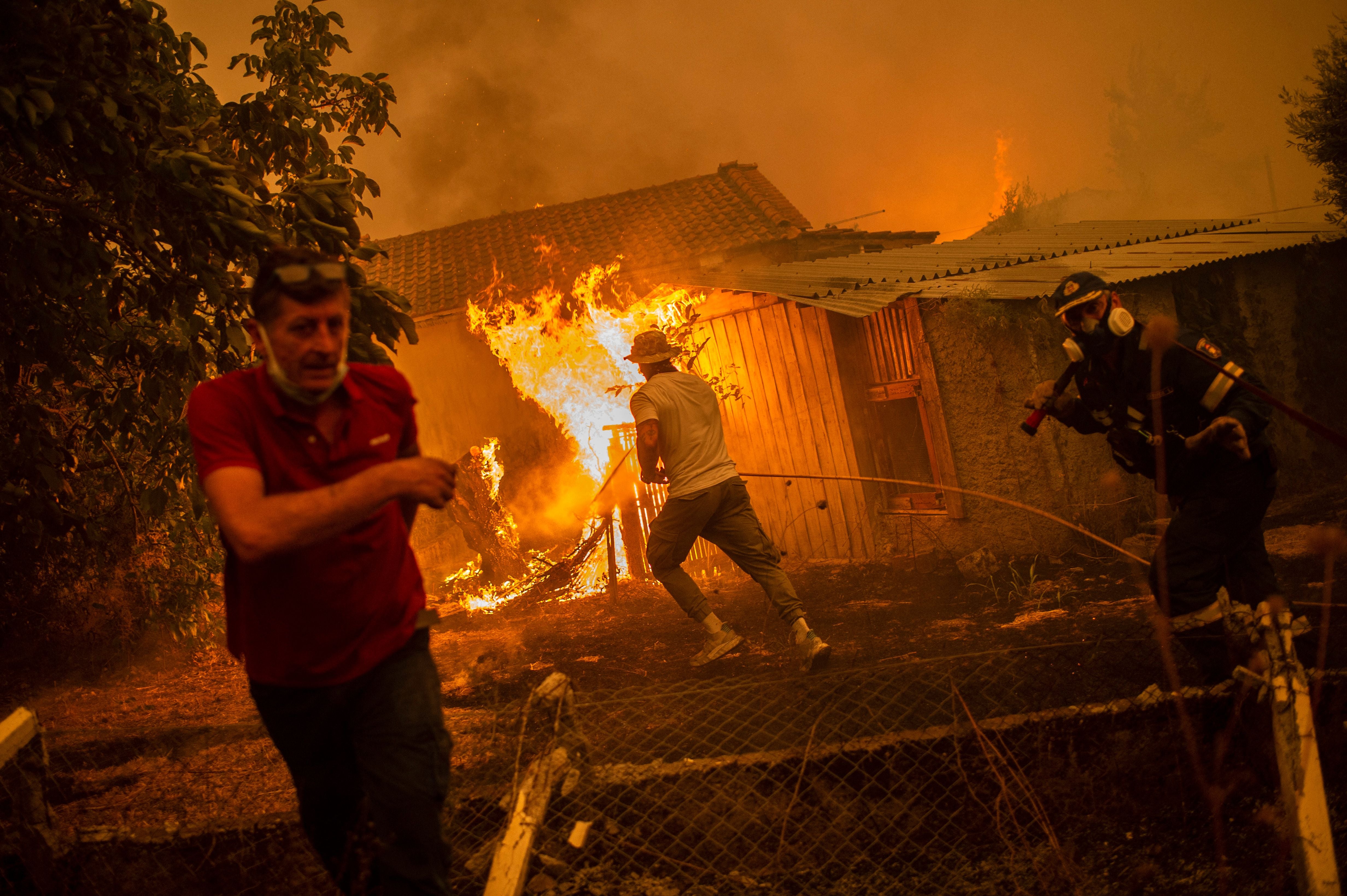 A firefighter and locals rush to a burning house in an attempt to extinguish forest fires that are approaching the village of Pefki on Evia (Euboea) island, Greece's second largest island, on August 8, 2021