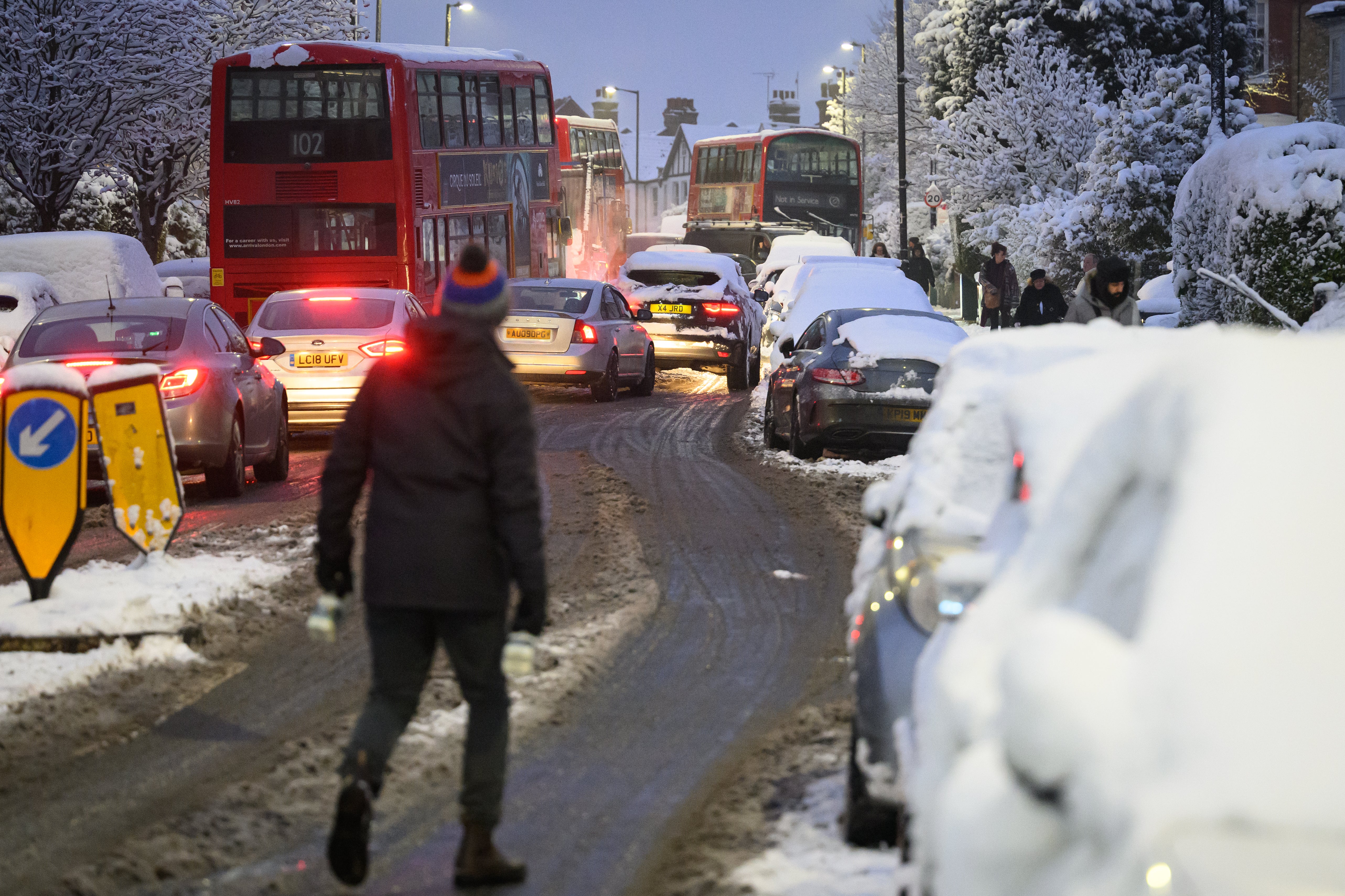 A man walks along an icy road as cars wind around abandoned buses on Monday