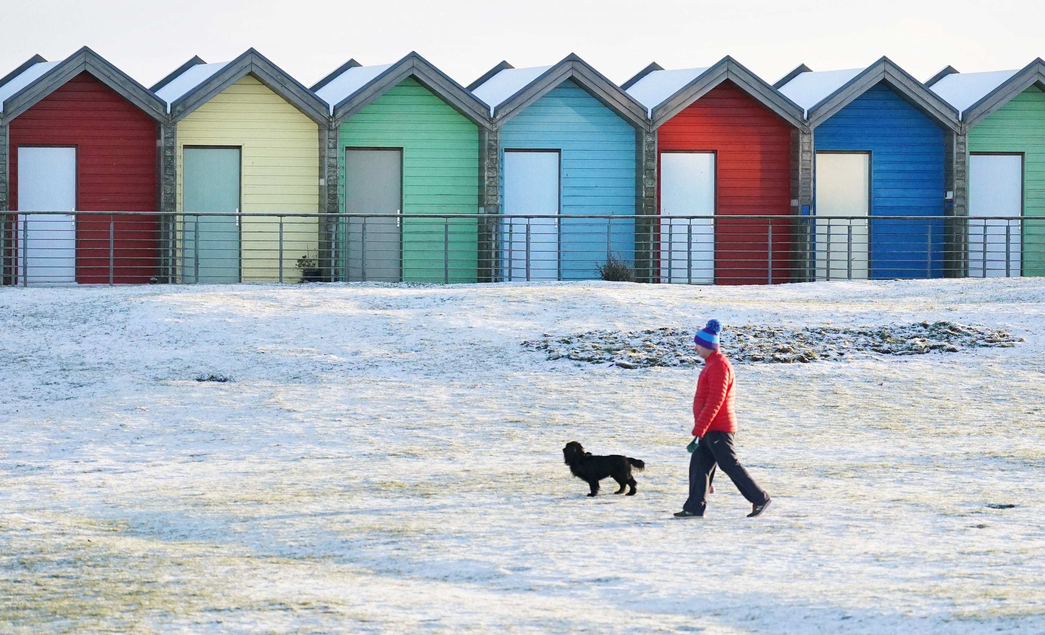 A man walks his dog near the beach huts on Blyth beach, Northumberland