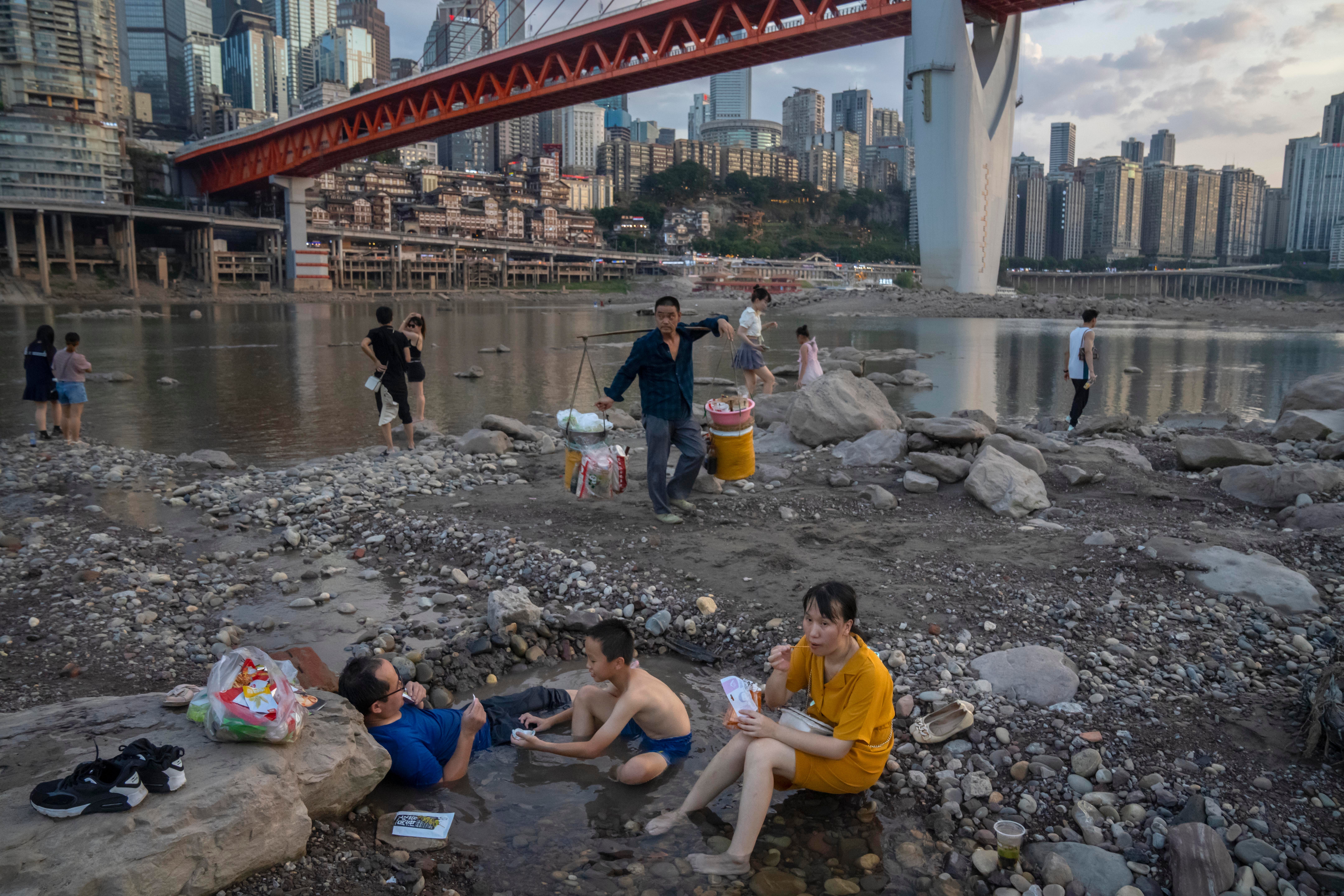 People sit in a shallow pool of water in the riverbed of the Jialing River, a tributary of the Yangtze, in southwestern China's Chongqing
