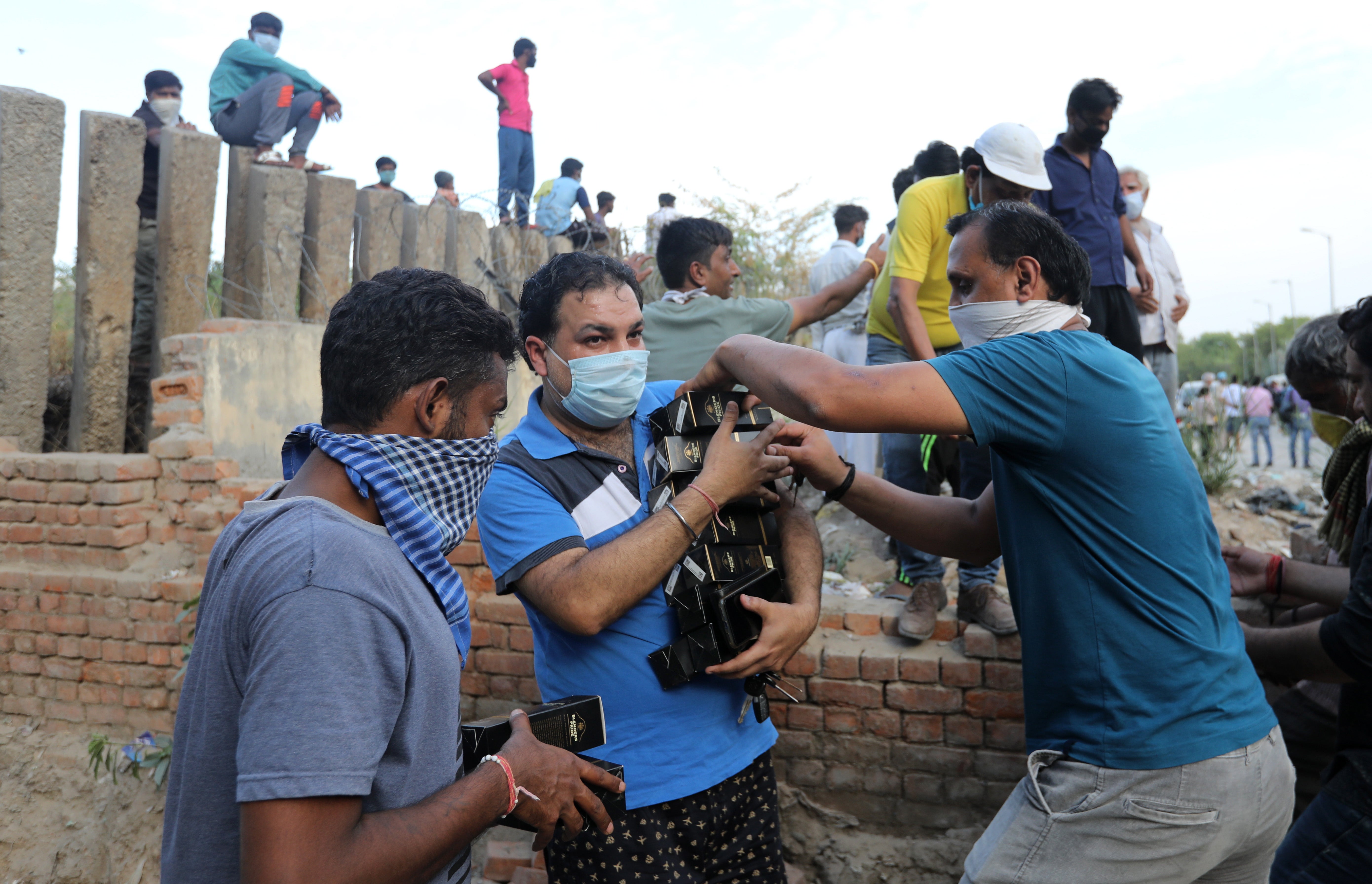 <p>Indian people wearing protective face masks after buying alcohol from a liquor shop</p>