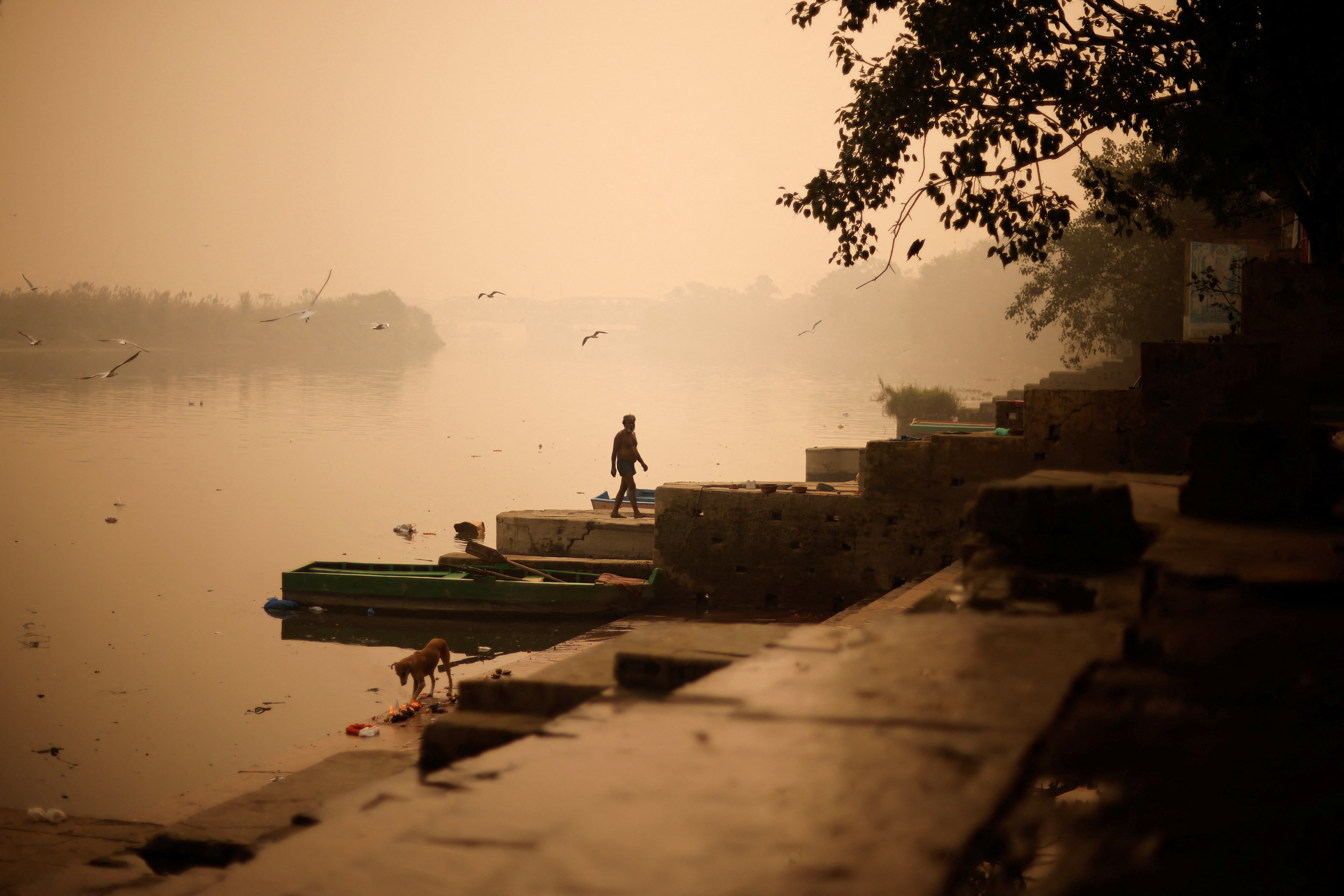 A Hindu man walks after praying as heavy smog covers the banks of the river Yamuna
