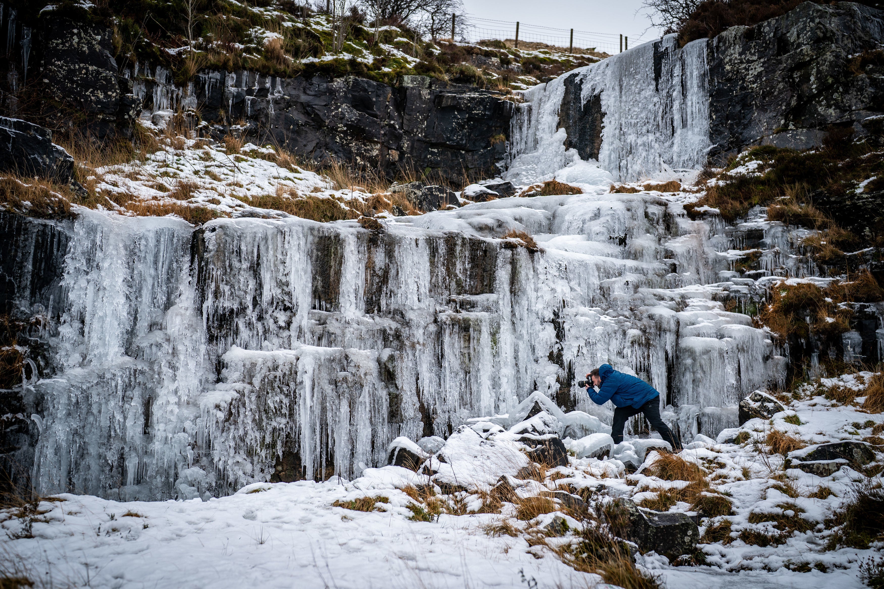 A man photographs icicle formations on a frozen waterfall in the Brecon Beacons National Park, Wales