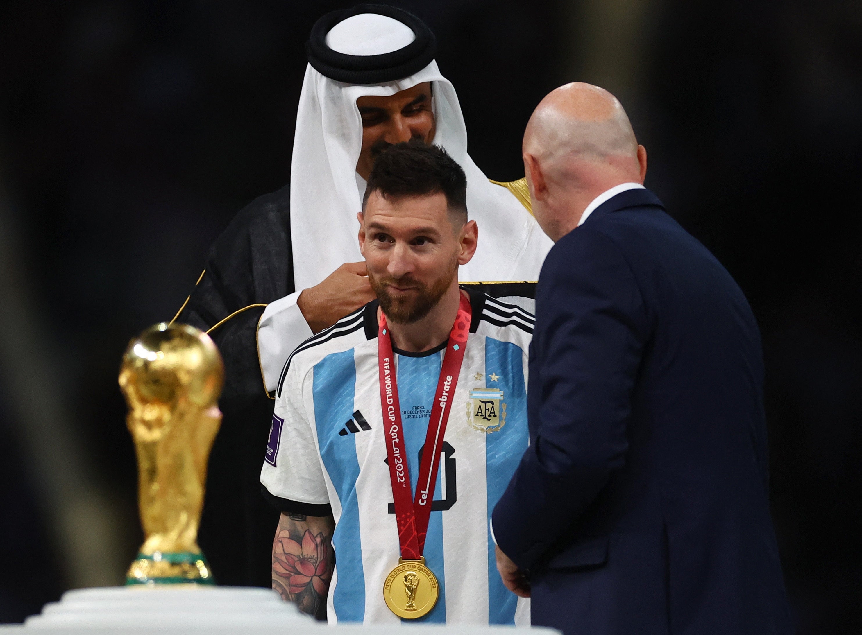 A robe is put on Lionel Messi by Emir of Qatar Sheikh Tamim bin Hamad Al Thani and Gianni Infantino during the trophy presentation