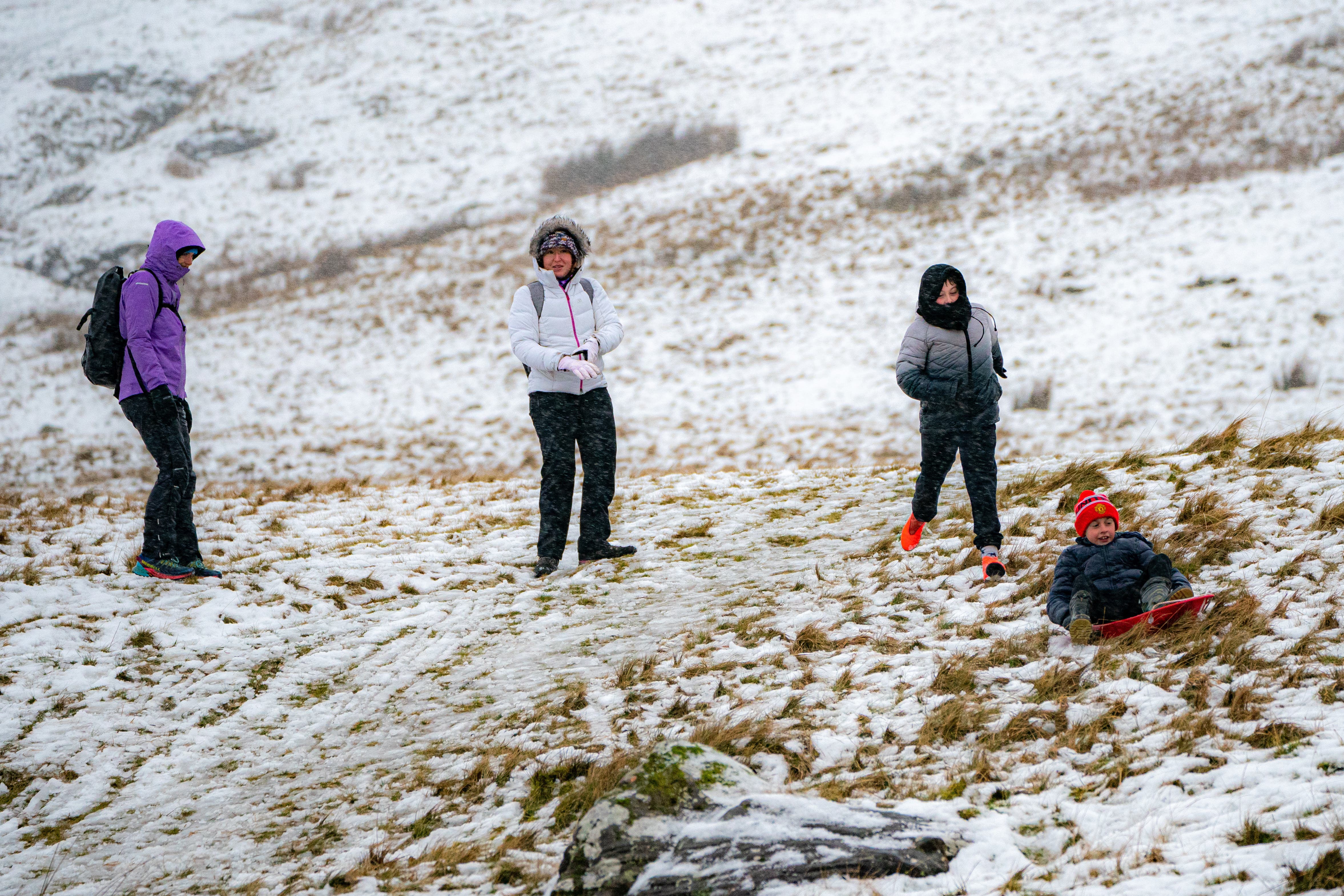 People make the most of the snow on an icy and snowy hill as rain falls in the Brecon Beacons National Park, Wales (PA)