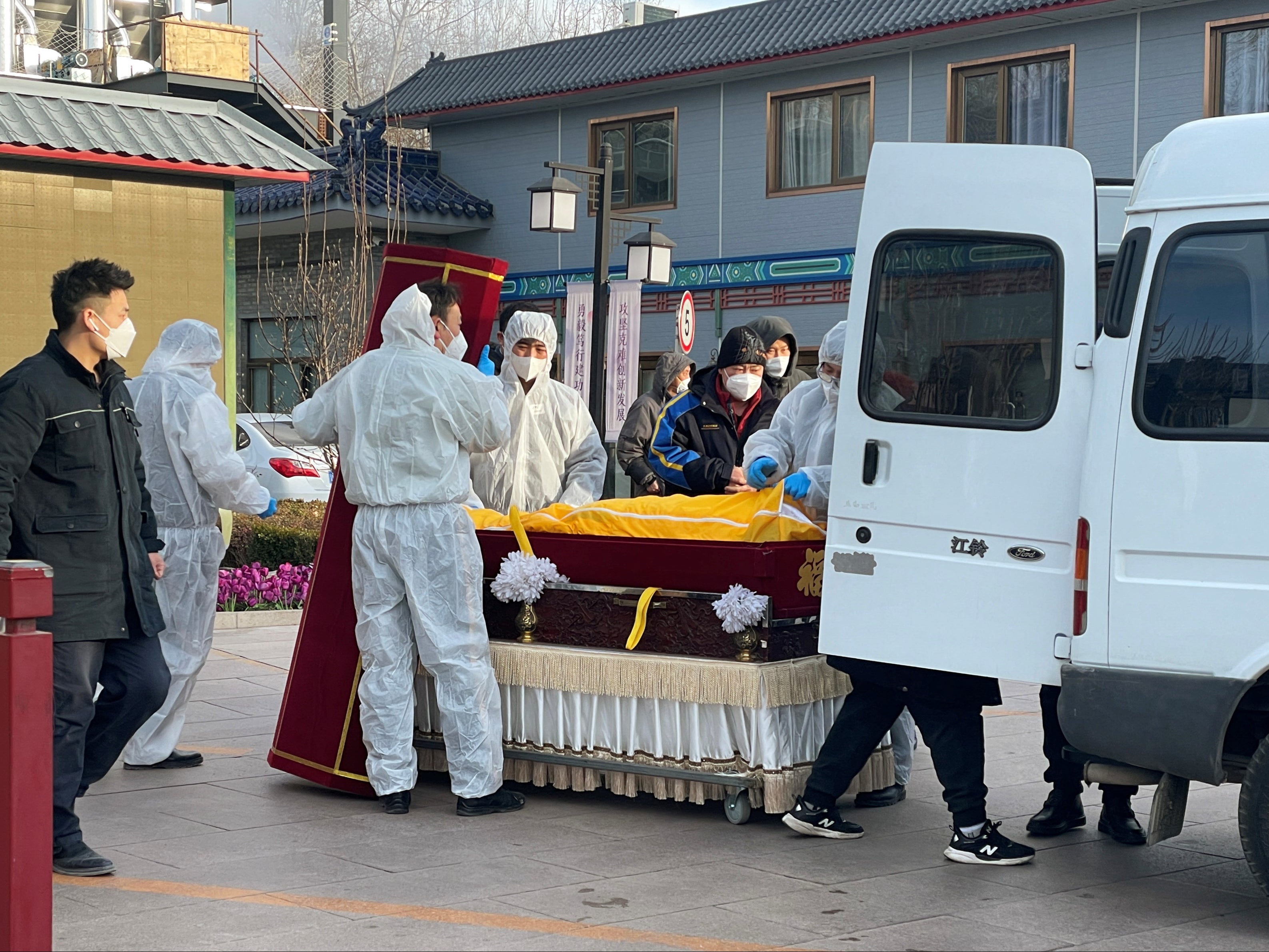 Workers in protective suits transfer a body in a casket at a funeral home