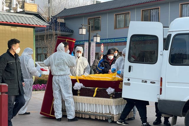 <p>Workers in protective suits transfer a body in a casket at a funeral home</p>