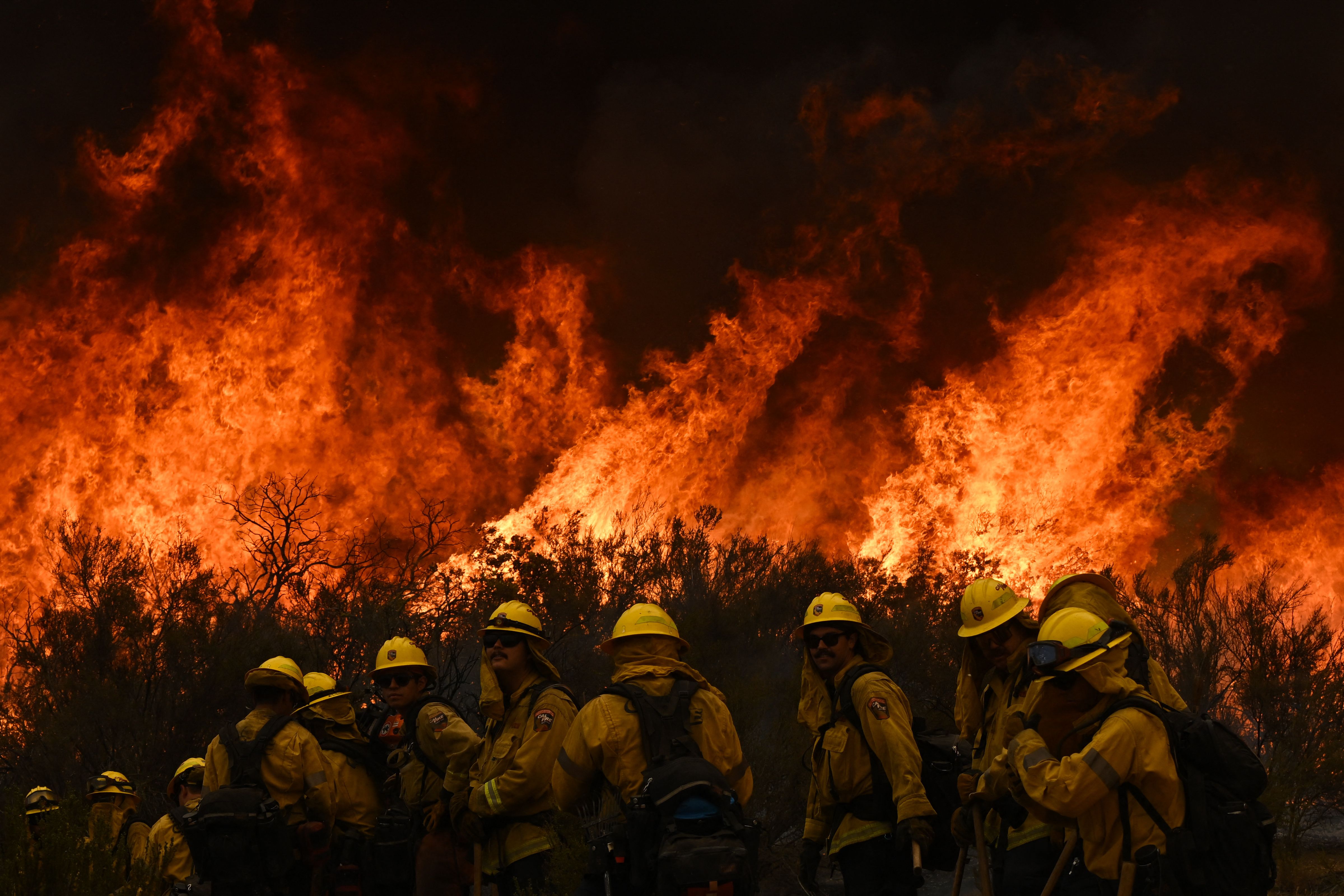 Firefighters turn away to watch for any stray embers during a firing operation to build a line to contain the Fairview Fire near Hemet, California, US