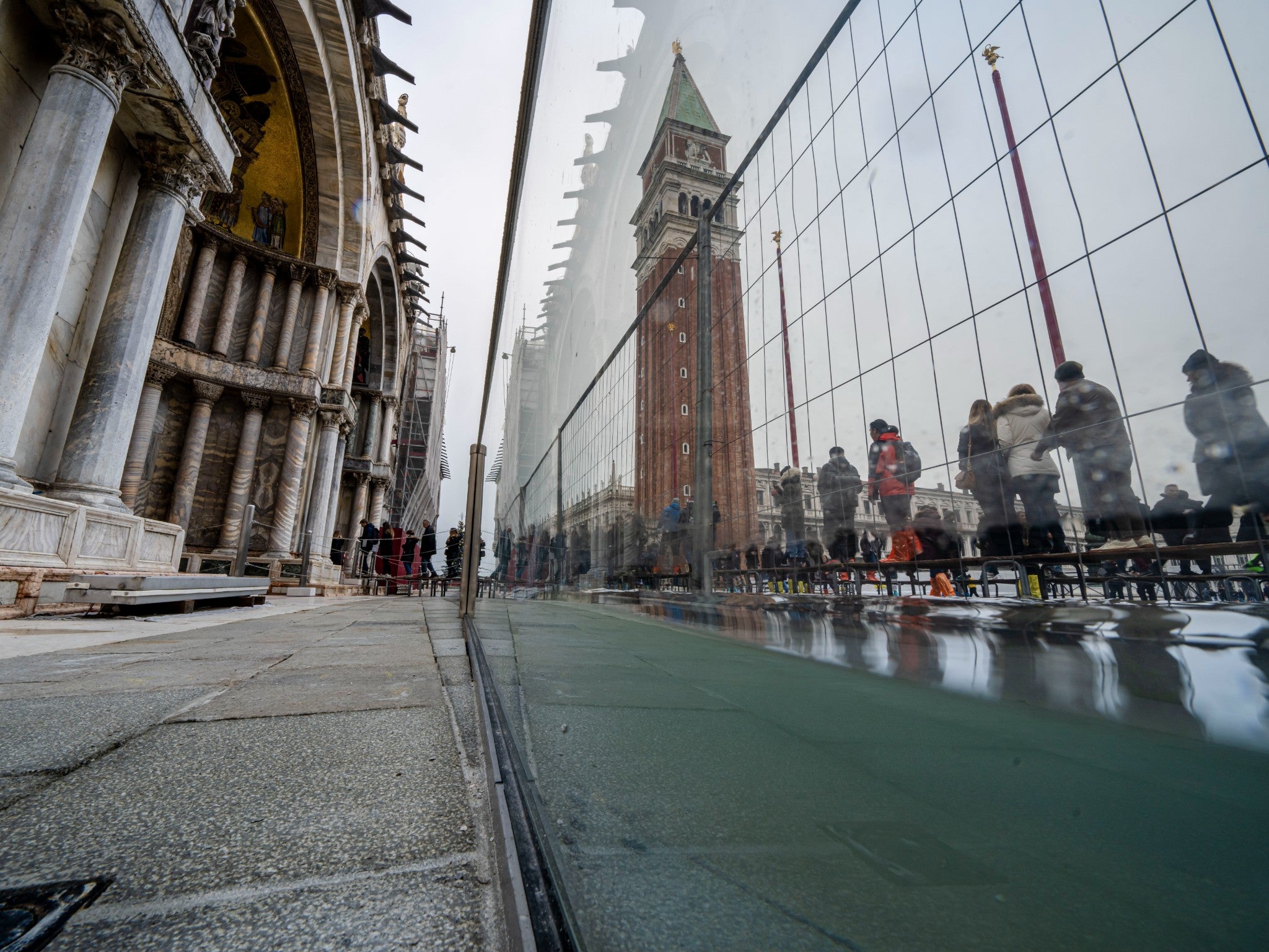 Tourists and residents walk on catwalks during a sea tide of around 97 centimeters (38.18 inches) to cross a flooded St. Mark's Square in Venice