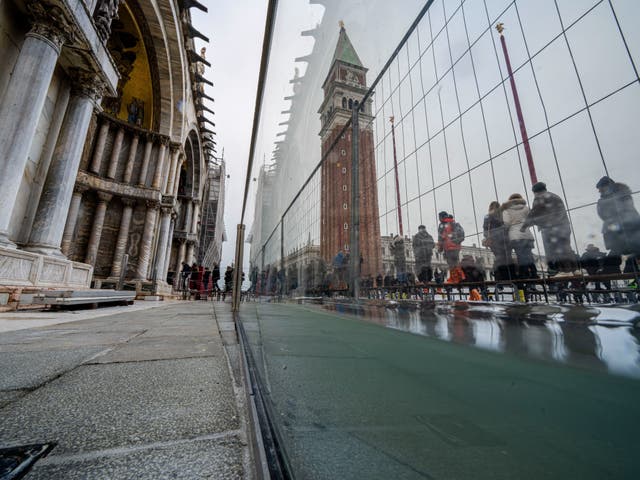 <p>Tourists and residents walk on catwalks during a sea tide of around 97 centimeters (38.18 inches) to cross a flooded St. Mark's Square in Venice</p>