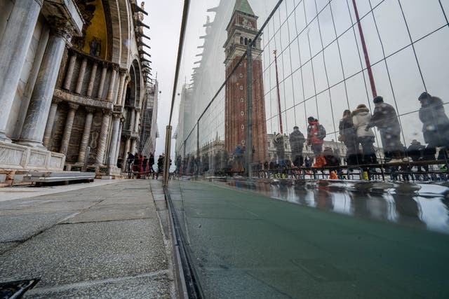 <p>Tourists and residents walk on catwalks during a sea tide of around 97 centimeters (38.18 inches) to cross a flooded St. Mark's Square in Venice</p>