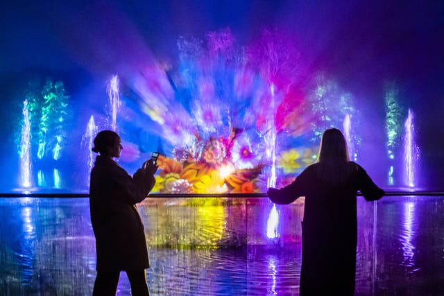 People view an installation that is projected onto water droplets over a lake, that forms part of the Enchanted Forest Winter Illuminations at Stockeld Park in Wetherby, North Yorkshire (Danny Lawson/PA)