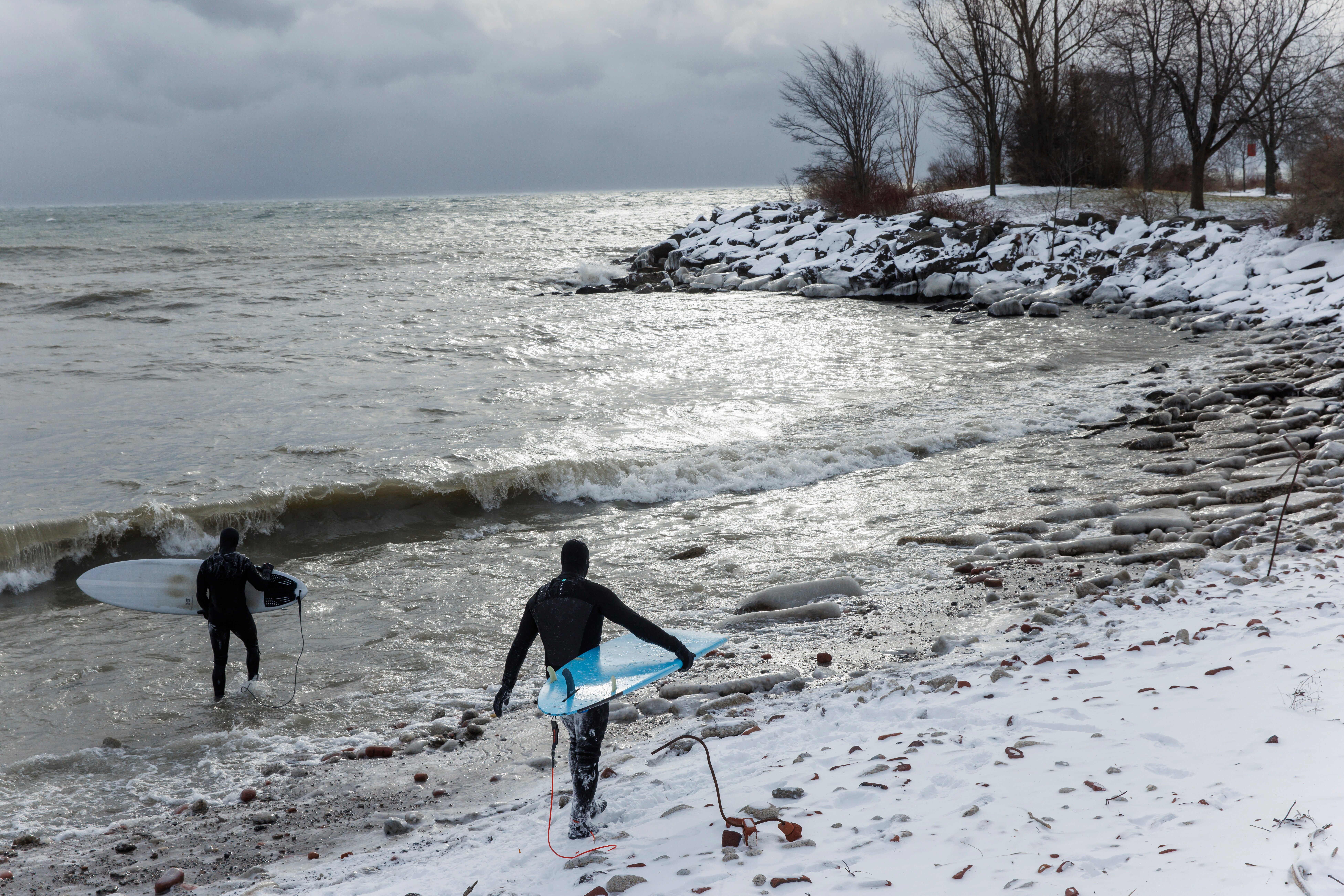 Surfers make their way out to Lake Ontario to surf the waves created by a major winter storm, in Toronto, Saturday, Dec. 24, 2022