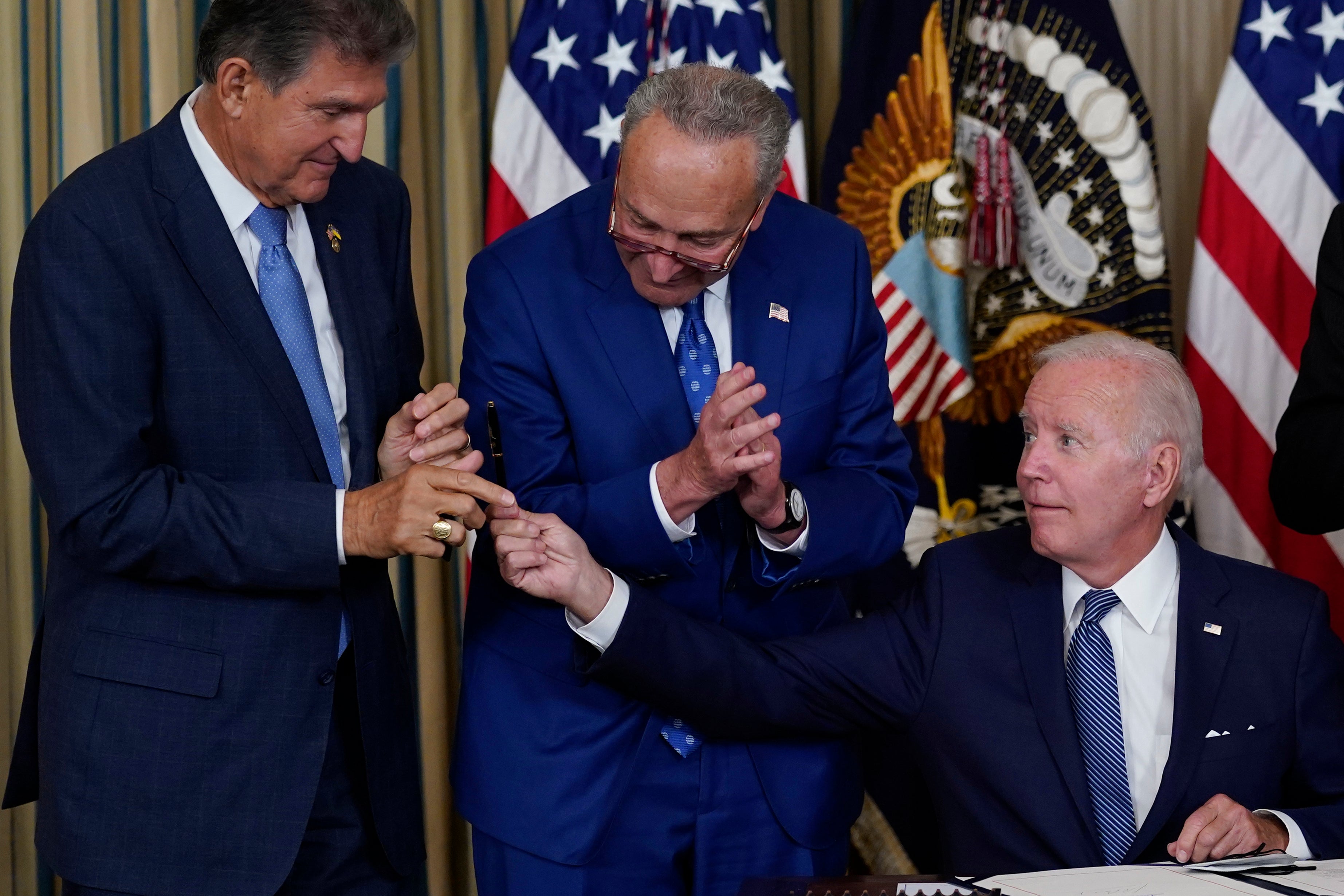 President Joe Biden hands the pen he used to sign the Democrats' landmark climate change and health care bill to Senator Joe Manchin as Senate Majority Leader Chuck Schumer looks on