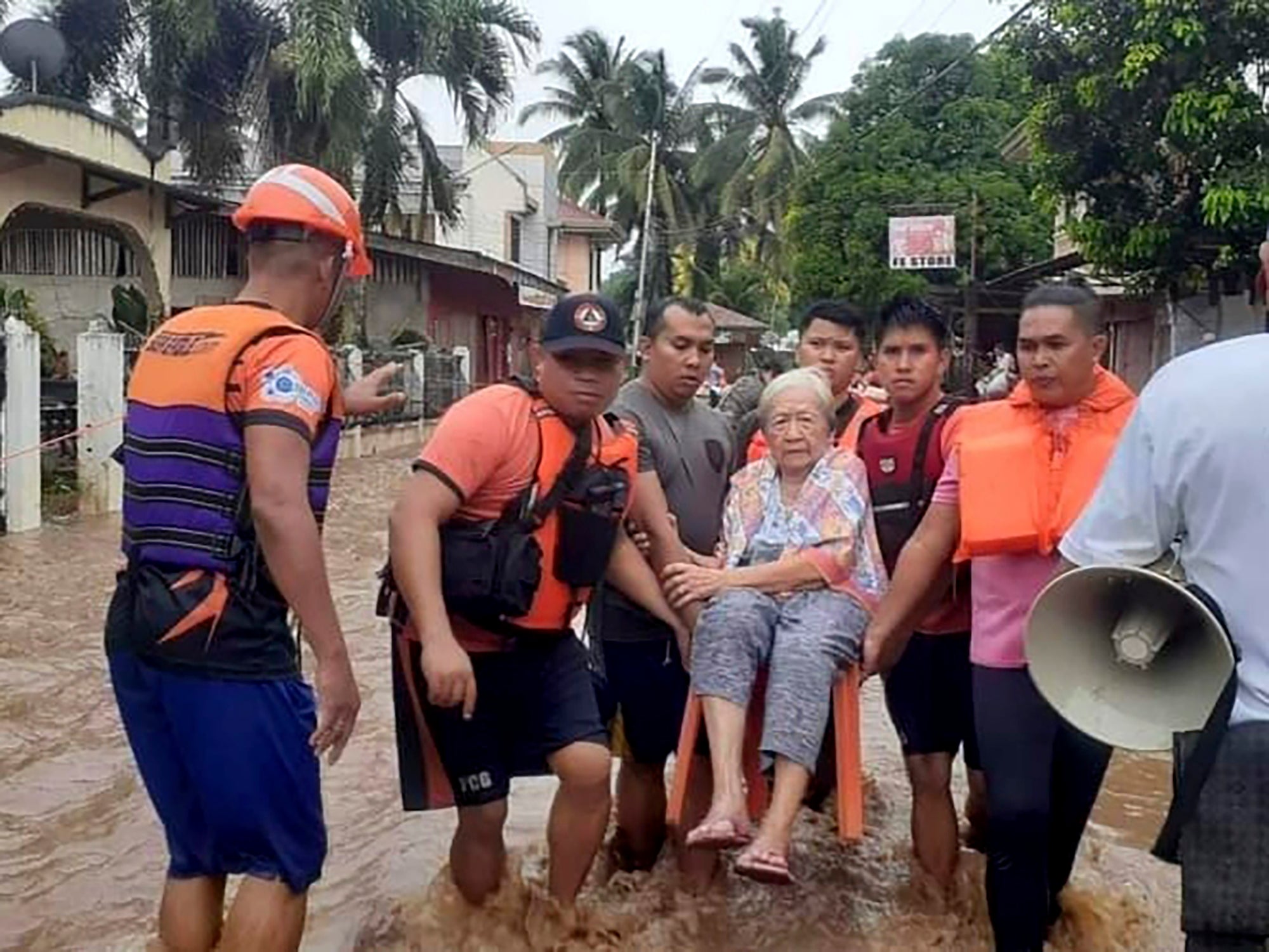 An elderly woman sits on a chair while being carried by coast guard personnel wading through floodwaters in Plaridel, Misamis Occidental province in the southern Philippines