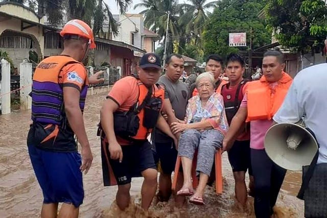 <p>In this image provided by the Philippine Coast Guard, an elderly woman sits on a chair while being carried by coast guard personnel wading through floodwaters in Plaridel, Misamis Occidental province in the southern Philippines, Monday, 26 December 2022</p>