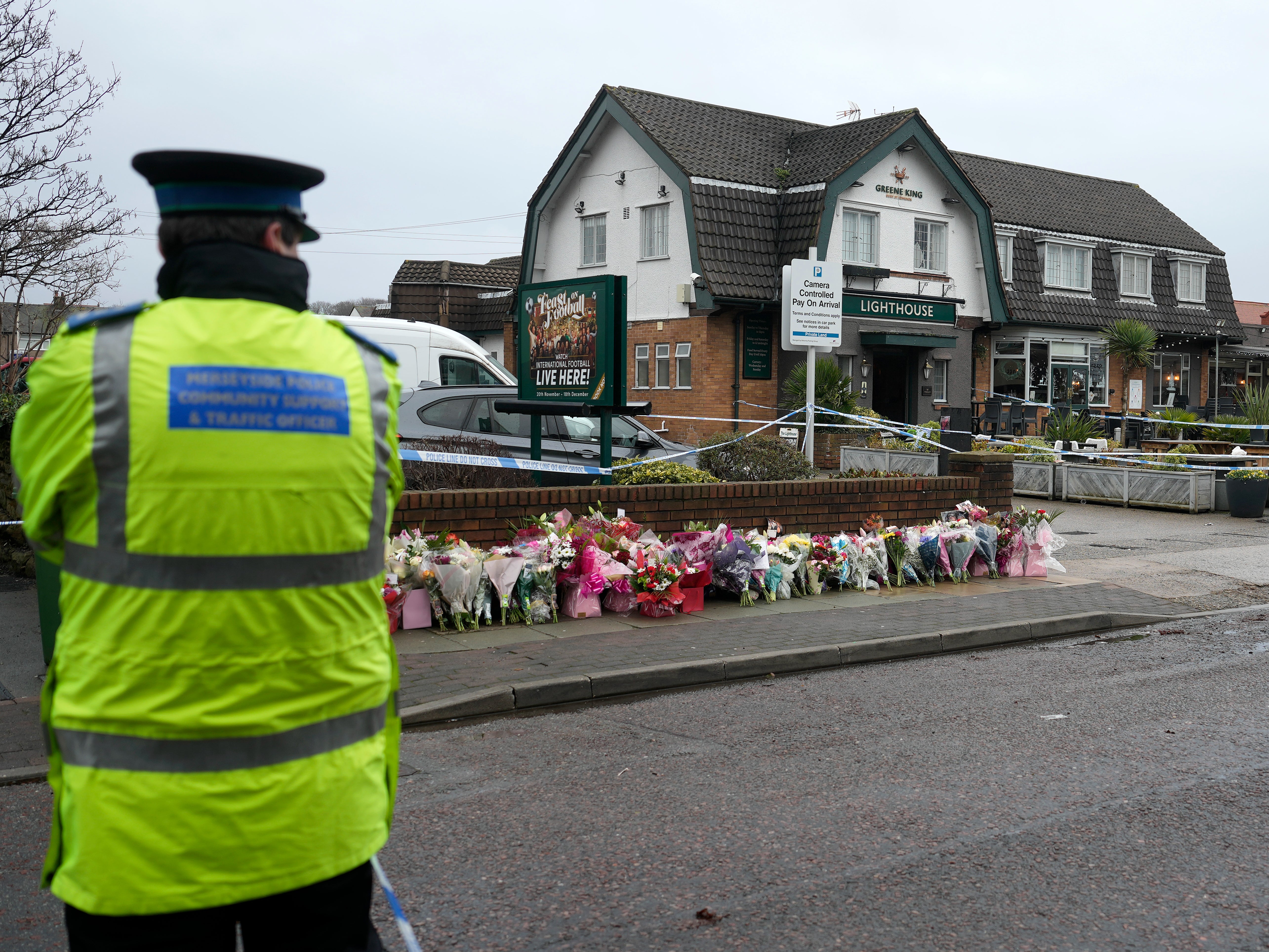 Police stand watch at the pub, where flowers were laid after the killing