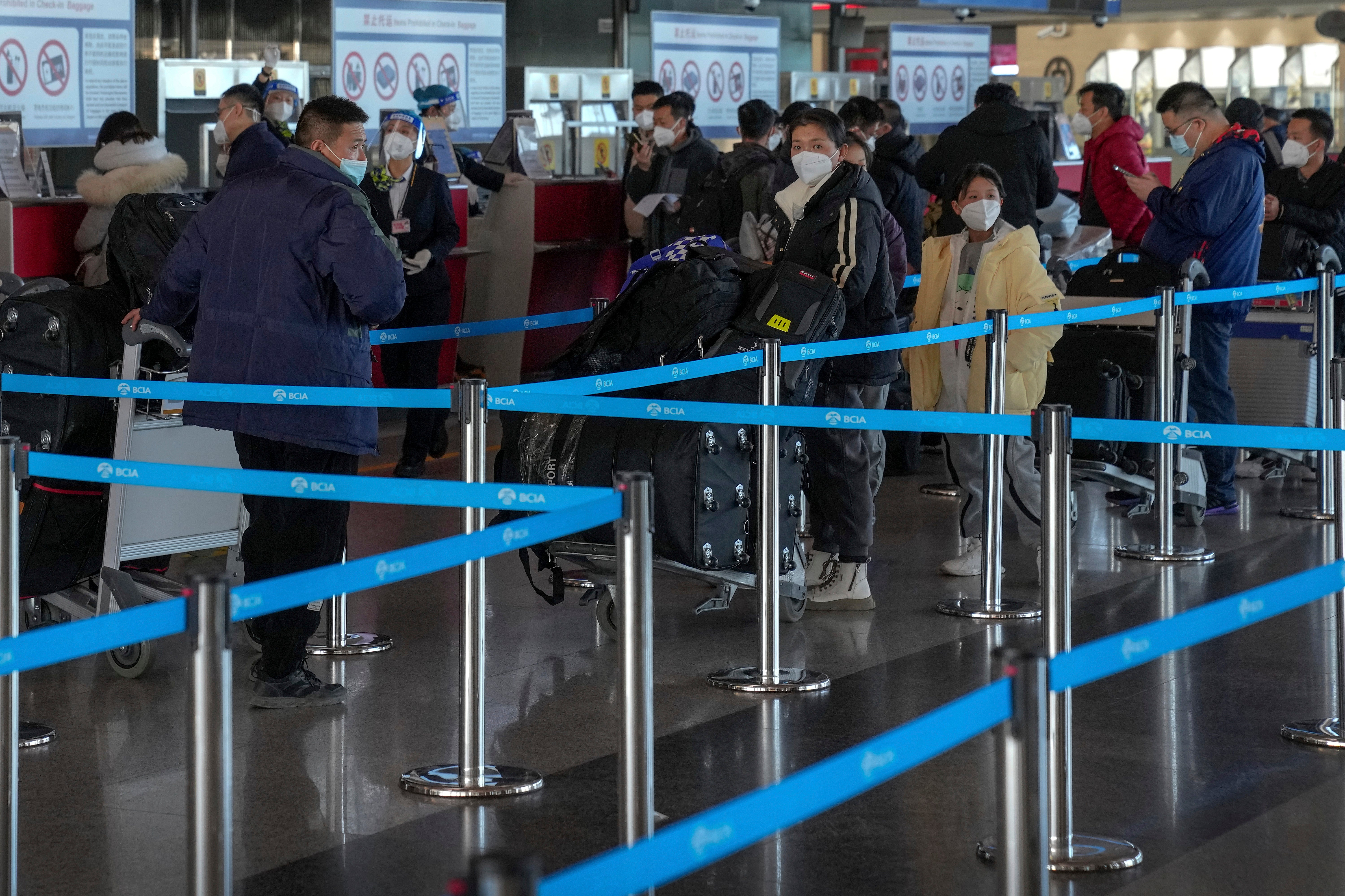 Masked travellers with luggage line up at the international flight check in counter at the Beijing Capital International Airport