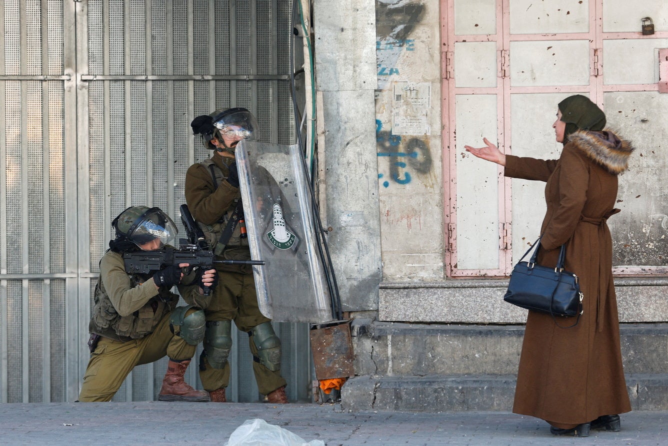 A Palestinian woman gestures in front of Israeli troops during a protest over the killing of three Palestinian gunmen by Israeli forces, in Hebron in the Israeli-occupied West Bank