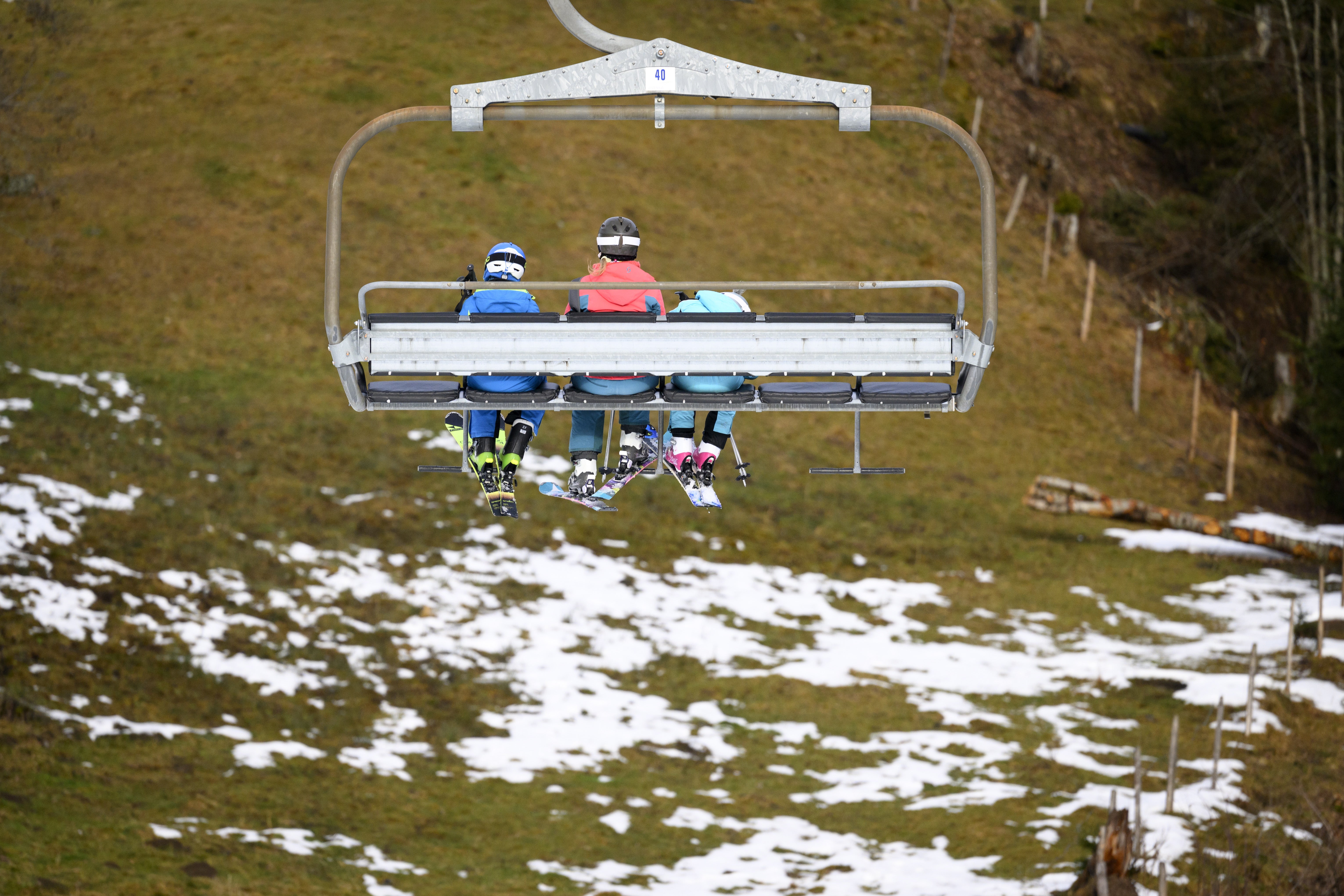 Skiers ride a chairlift between La Rasse et Chaux Ronde above a snowless field