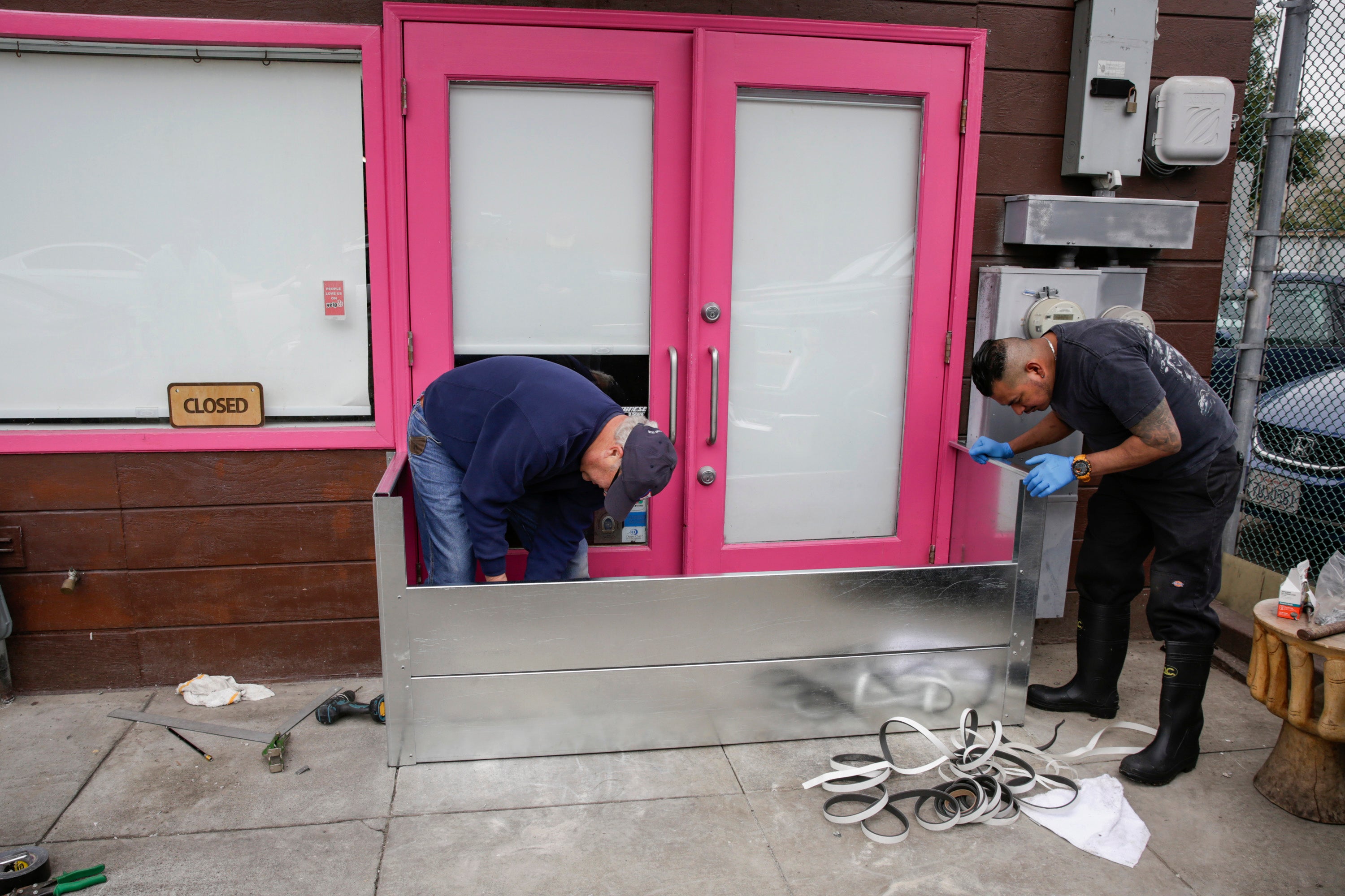 Angelo Coric and Feliciano Cinta, right install a metal flood gate in front of Pink Onion, a pizzeria in the Mission District in San Francisco, on Tuesday in preparation of storms. Pink Onion saw serious flooding and damage on Saturday in the wake of a storm