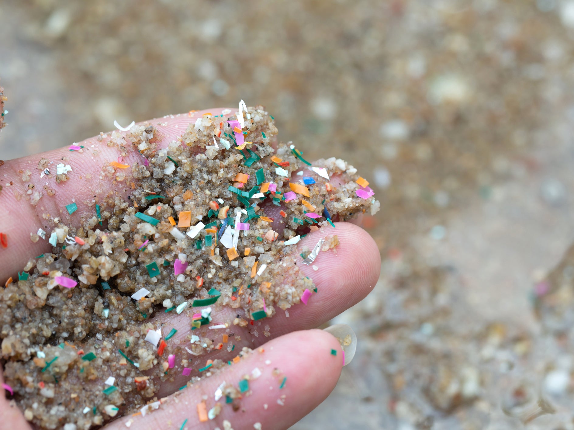 Microplastics have been found deep inside the ocean and mixed with sand. This close-up side shot of hands shows microplastic waste contaminated with the seaside sand
