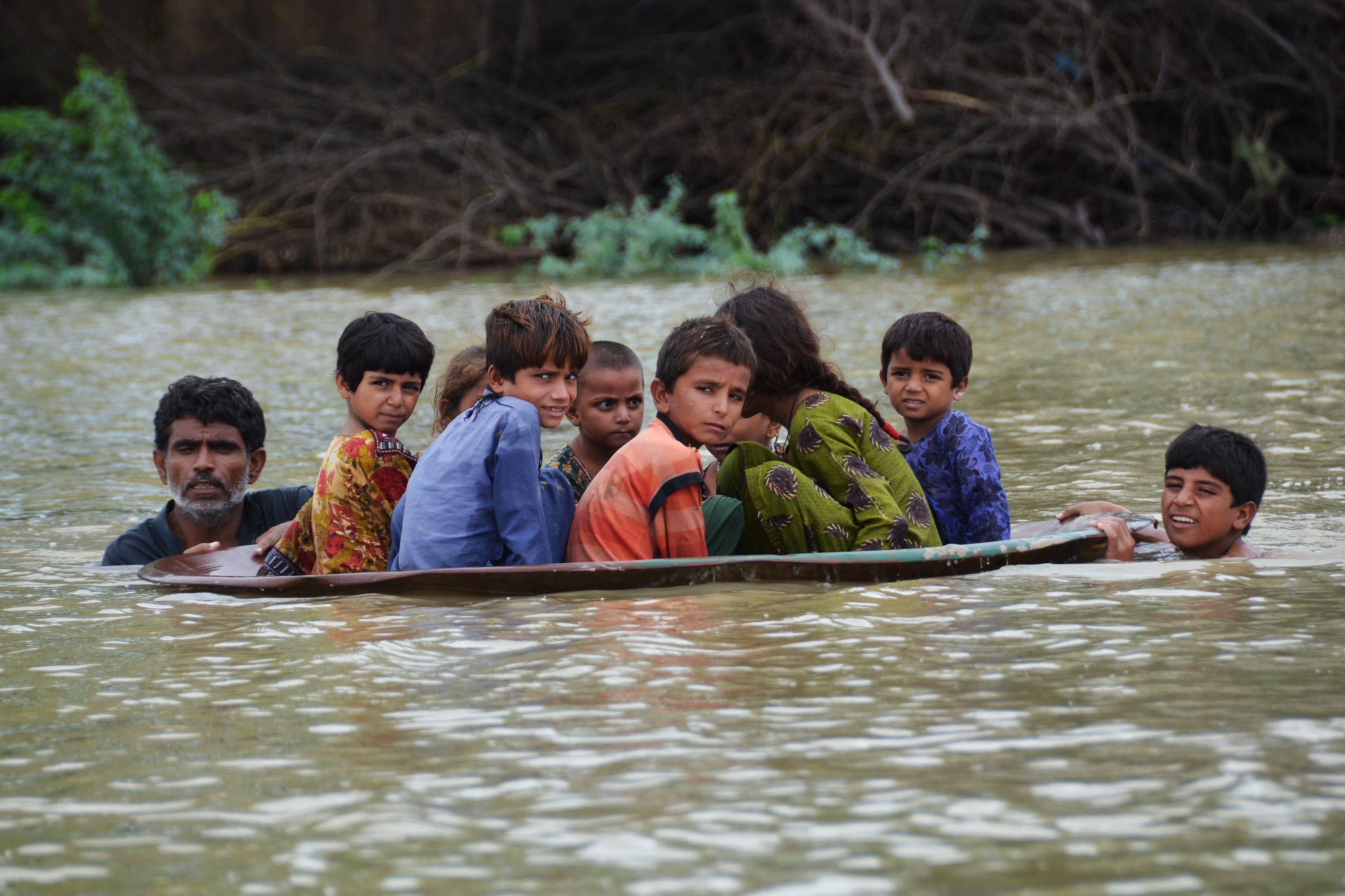 File. A man (L) along with a youth use a satellite dish to move children across a flooded area after heavy monsoon rainfalls in Jaffarabad district, Balochistan province, on 26 August 2022