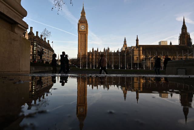 <p>Pedestrians are reflected in a puddle of rain water opposite the Houses of Parliament</p>
