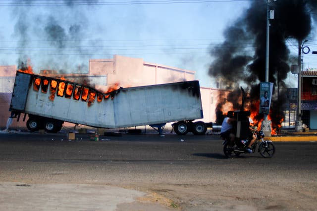 <p>Men ride on a motorcycle past a burning truck on the streets of Culiacan, Sinaloa state, Thursday, Jan. 5, 2023. </p>