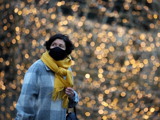 <p>A woman wears a Covid-19 face mask as she walks past Christmas lights</p>