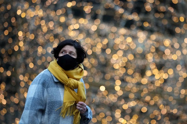 <p>A woman wears a Covid-19 face mask as she walks past Christmas lights</p>