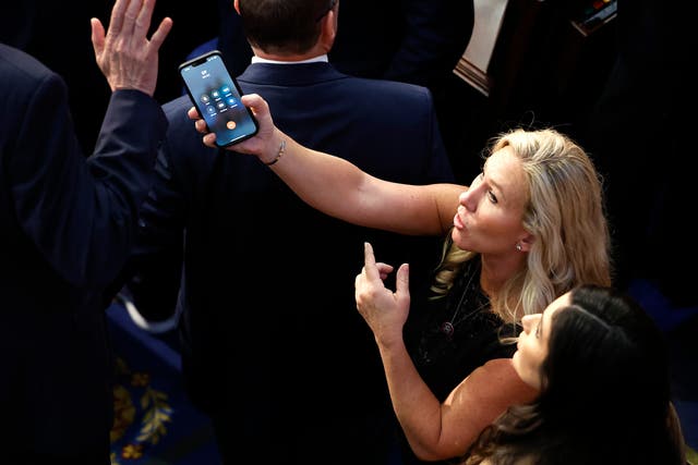 <p>US representative-elect Marjorie Taylor Greene offers a phone to Matt Rosendale in the House Chamber during the fourth day of voting for Speaker of the House at the US Capitol Building on 6 January 2023 in Washington, DC</p>