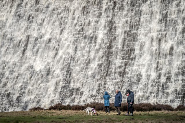 People look on as water pours down the front of Derwent Dam in Derbyshire, ahead of a Met Office yellow weather warning for rain for parts of the UK on Tuesday (PA)