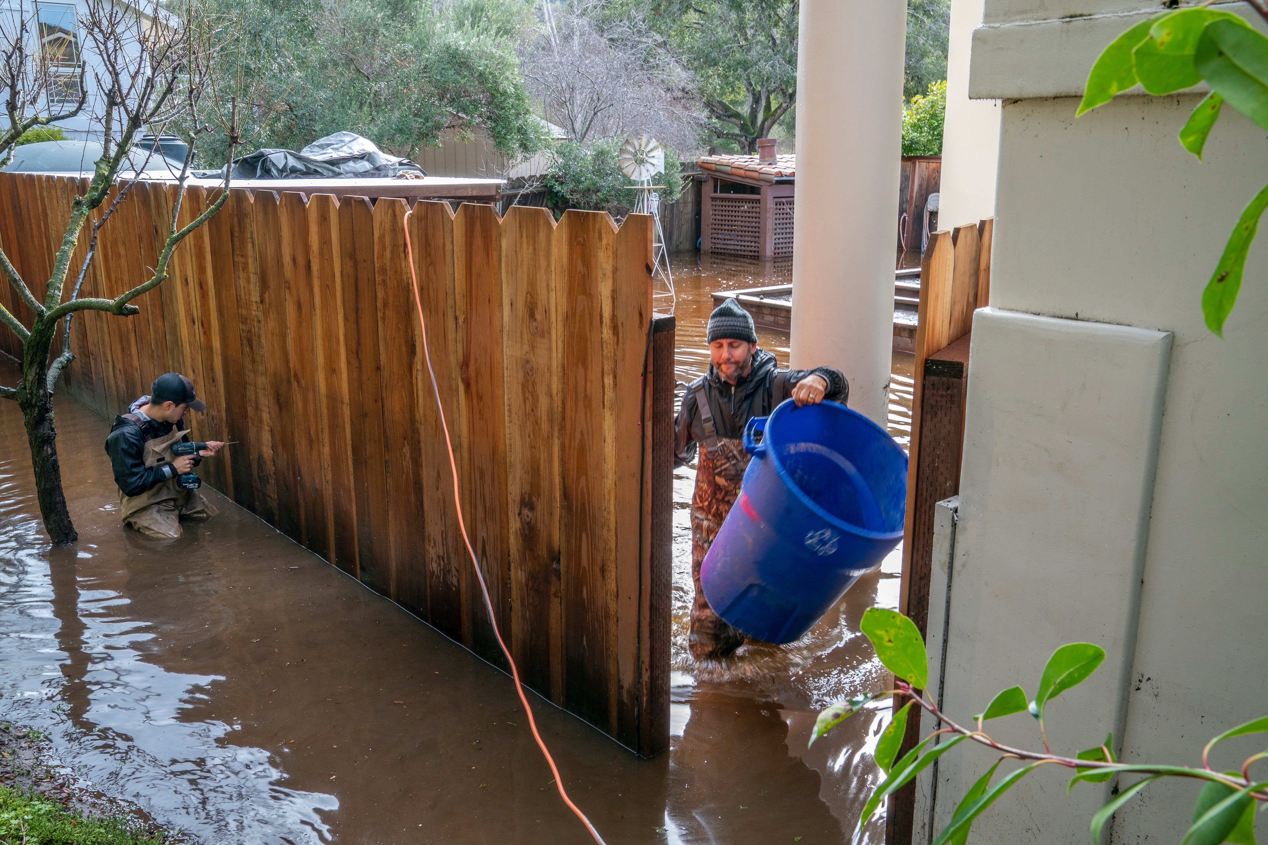 Residents help to clear water out of a flooded back yard on Paso Honda