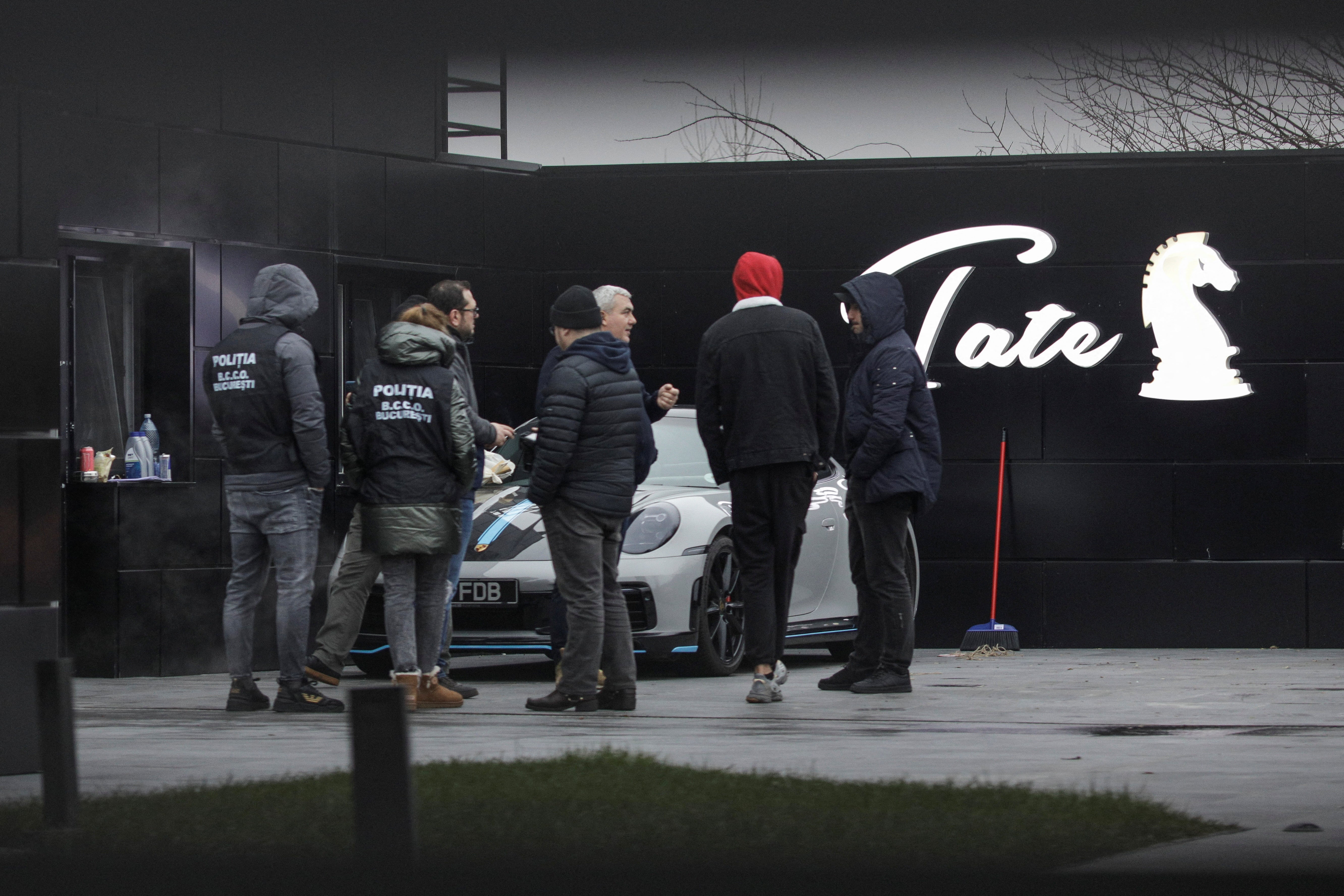 Romanian officials watch as the cars are taken away from Andrew Tate’s compound