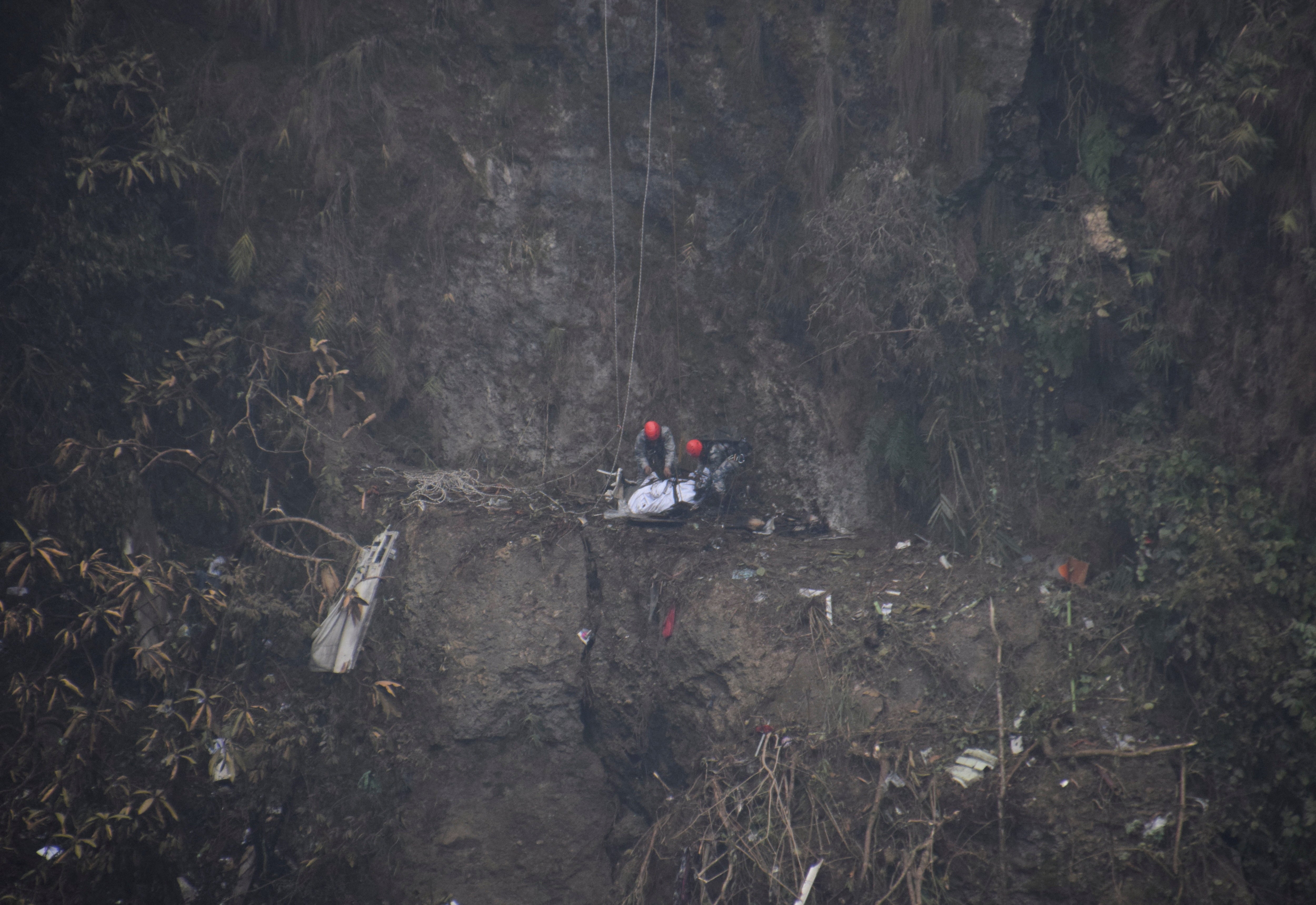 A rescue team works to recover the body of a victim from the site of the plane crash of a Yeti Airlines operated aircraft