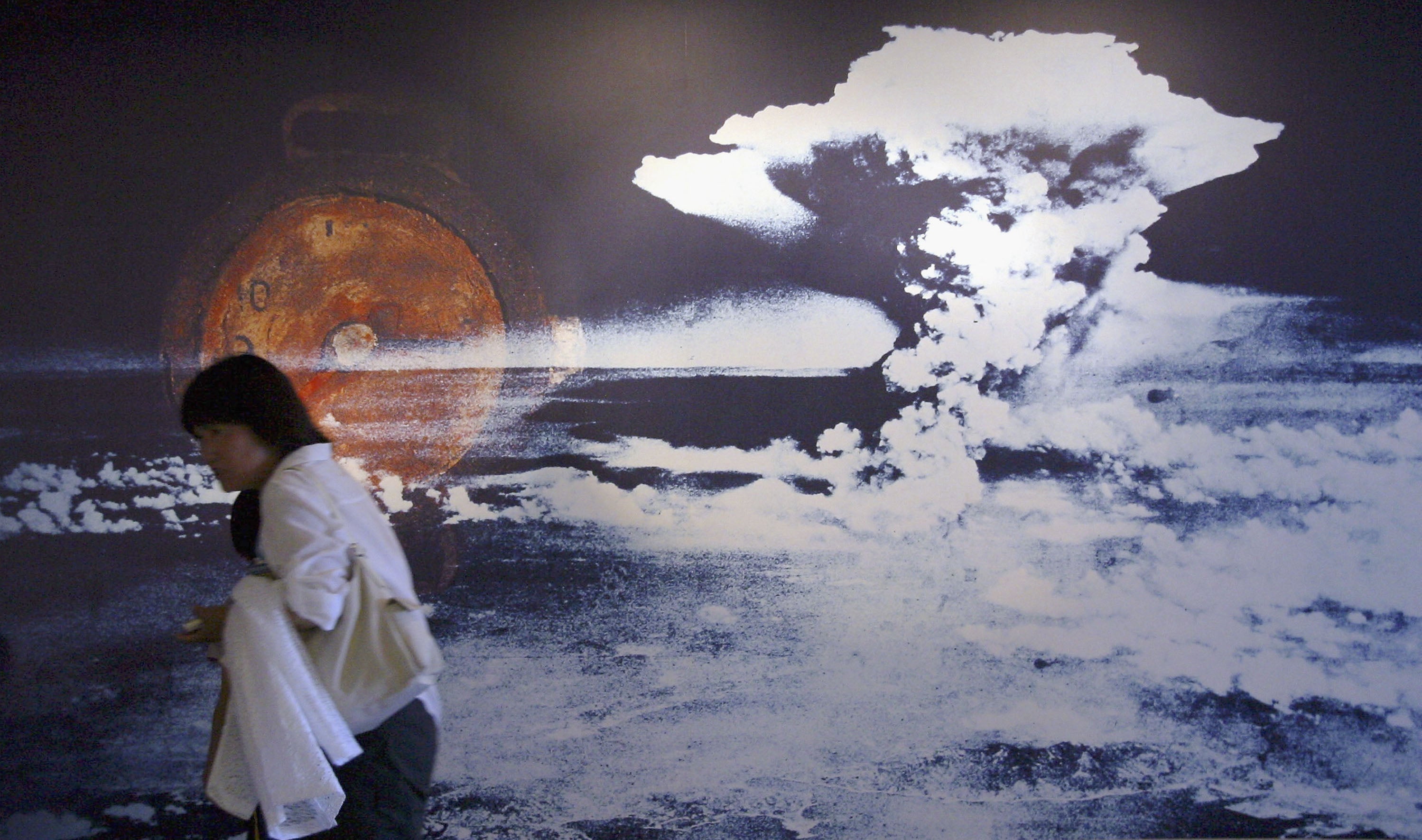 A visitor passes by a wall displaying a picture of the mushroom cloud