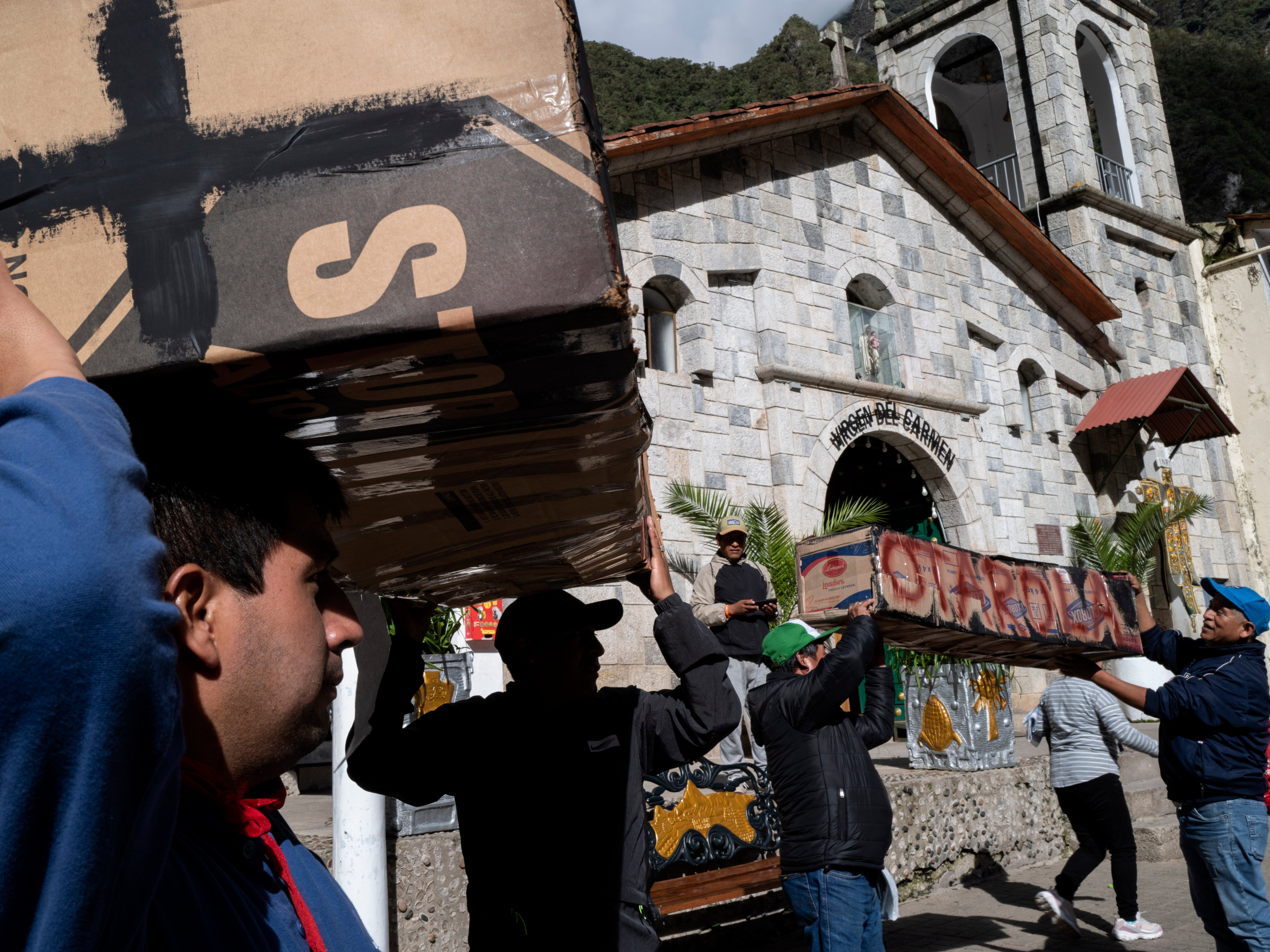 Residents and demonstrators carry symbolic cardboard coffins through the main plaza of the town