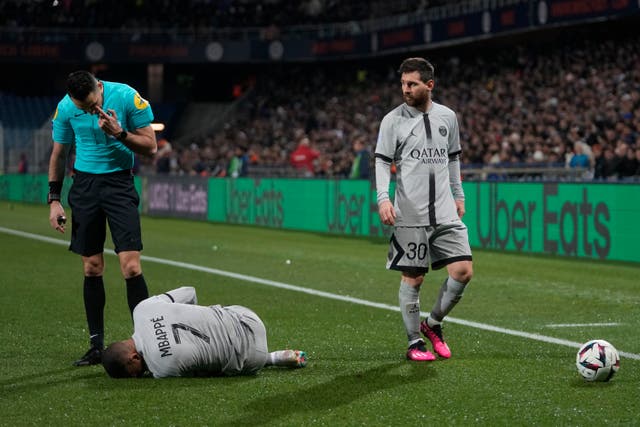 <p>Kylian Mbappe writhes on the floor as Lionel Messi looks on</p>