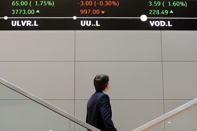 A man looks up at electronic ticker tape showing the FTSE 100 inside the London Stock Exchange (Nick Ansell/PA)